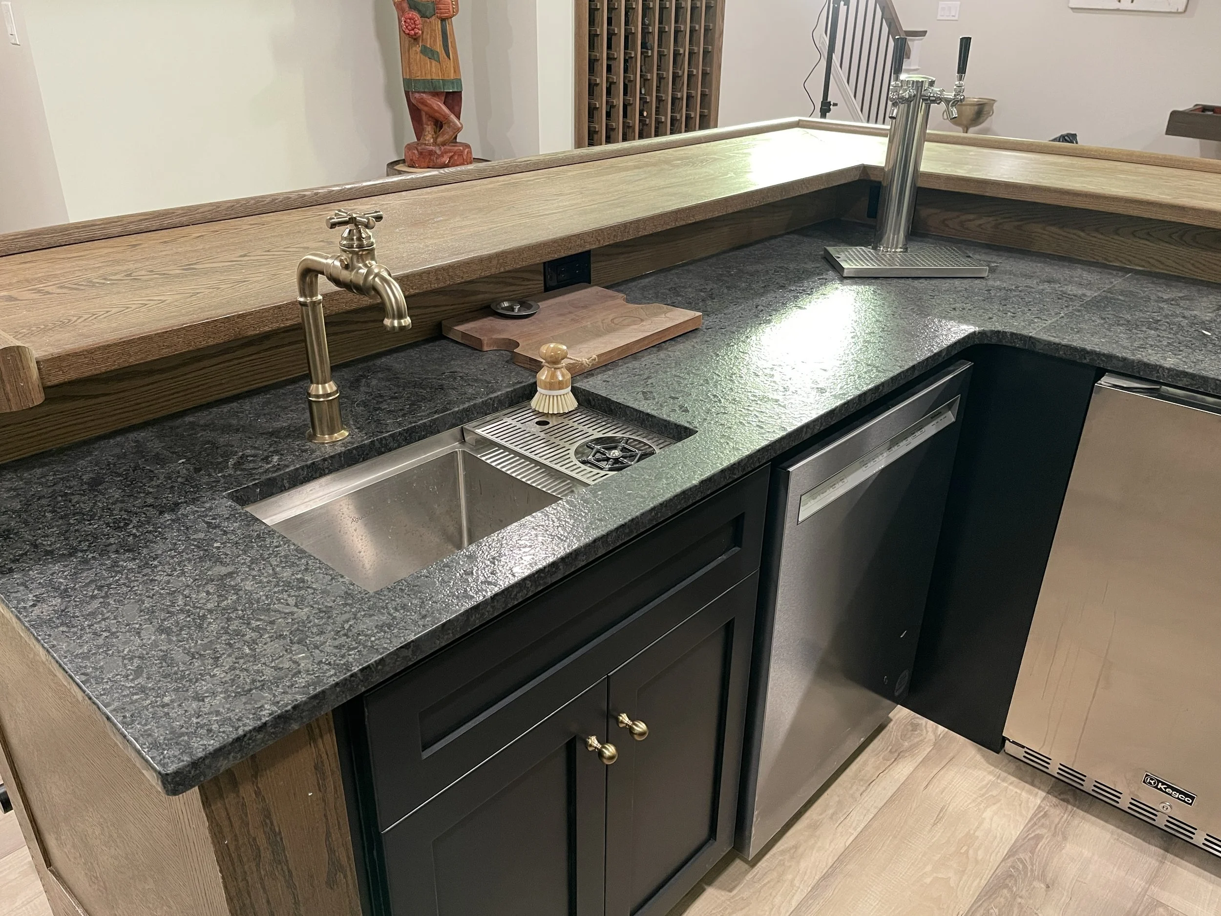 Detail of a granite bar countertop with a dual duty sink and cup rinse.  The brass faucet features an industrial cross handle, designed and photographed by Sara Trotter / Chroma Maison Design.