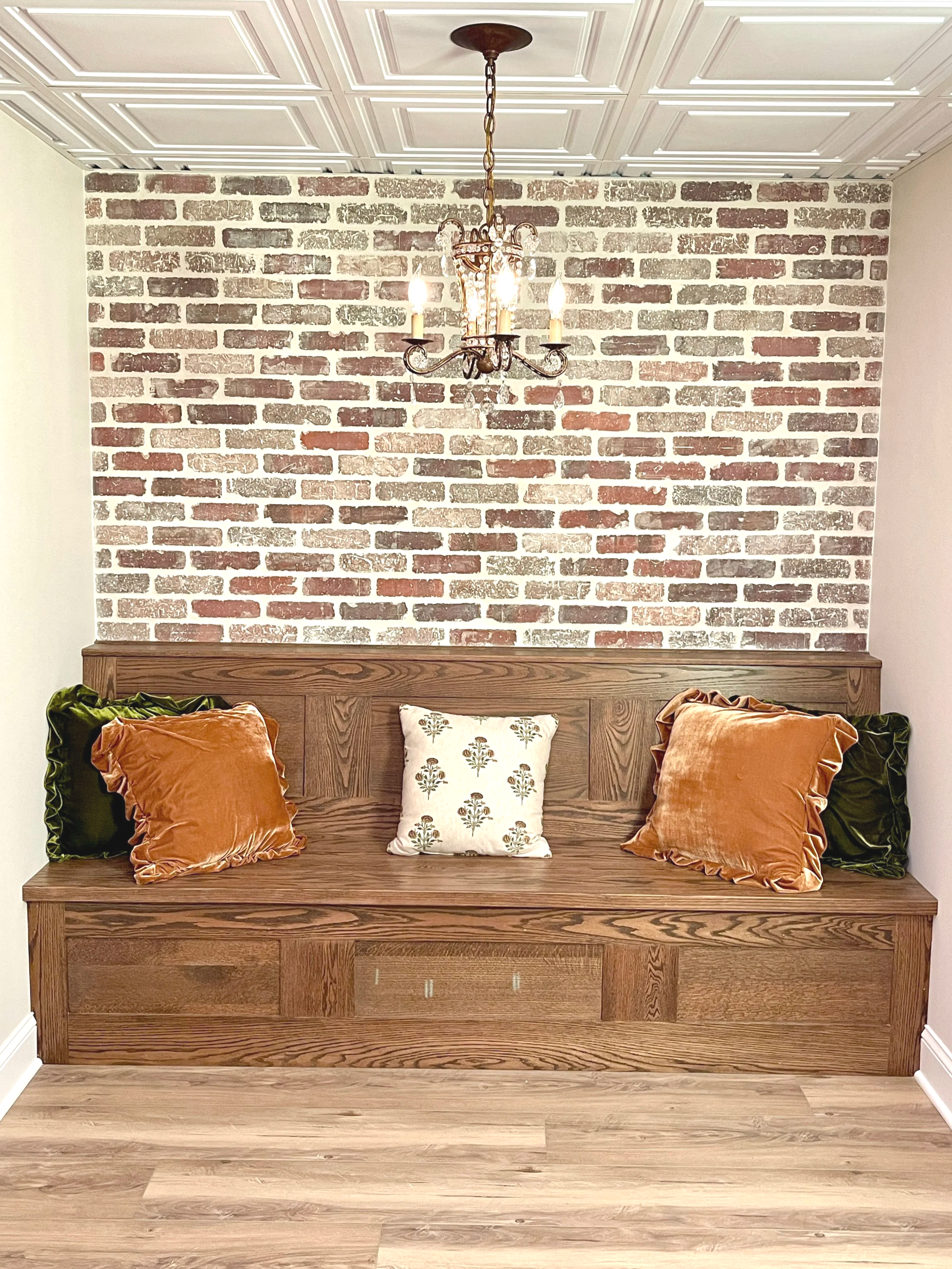 Custom antique-style walnut bar bench against a brick accent wall and a vintage French chandelier, designed and photographed by Sara Trotter / Chroma Maison Design.