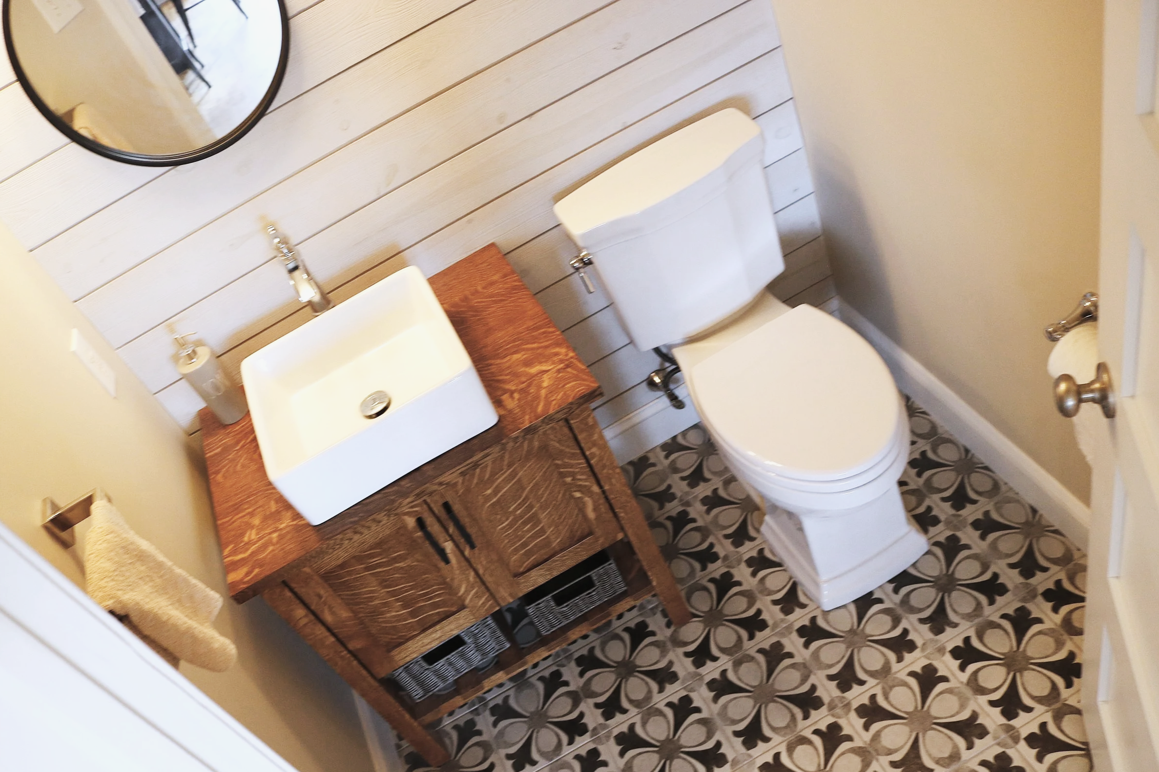 Farmhouse powder room with a vessel sink a top a tiger oak custom vanity.  Complete with a shiplap accent wall and a nostalgic pattern tile floor, designed and photographed by Sara Trotter / Chroma Maison Design.