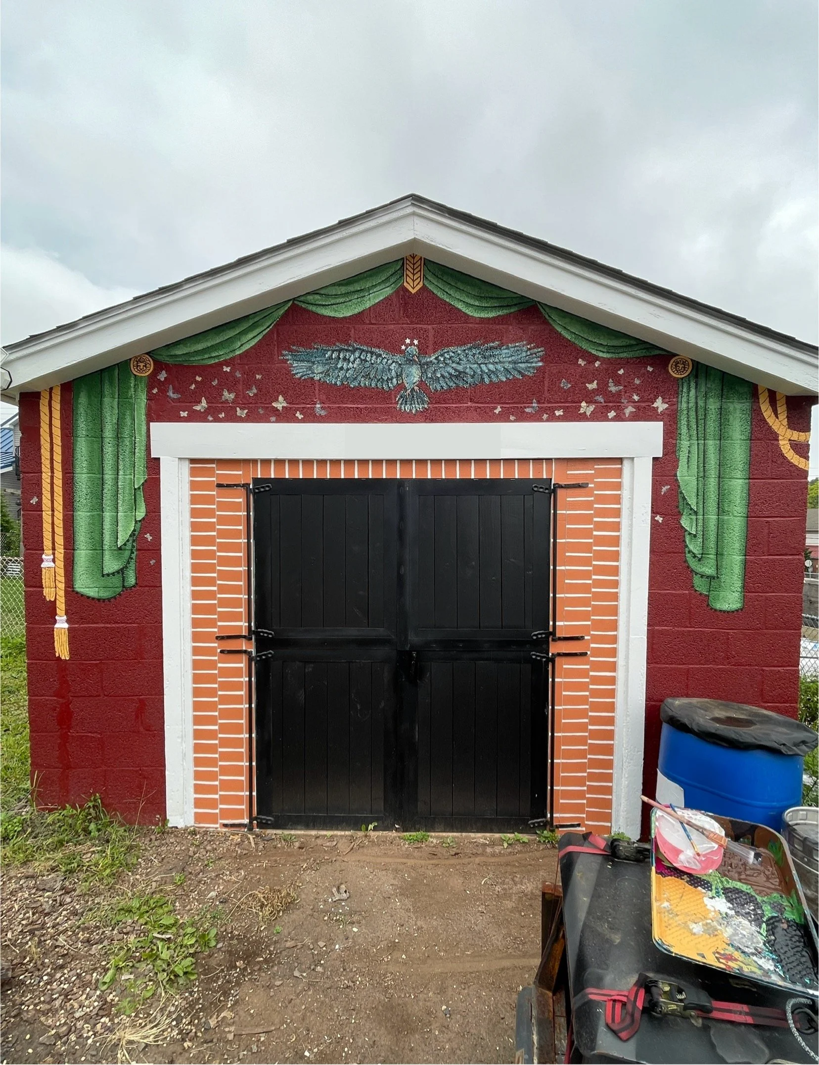 Garage with hand-painted green theatre curtains, faux painted brick, and a star crowned crow with wings spread surrounded by a burst of moths, designed and painted By Sara Trotter / Chroma Maison Design.