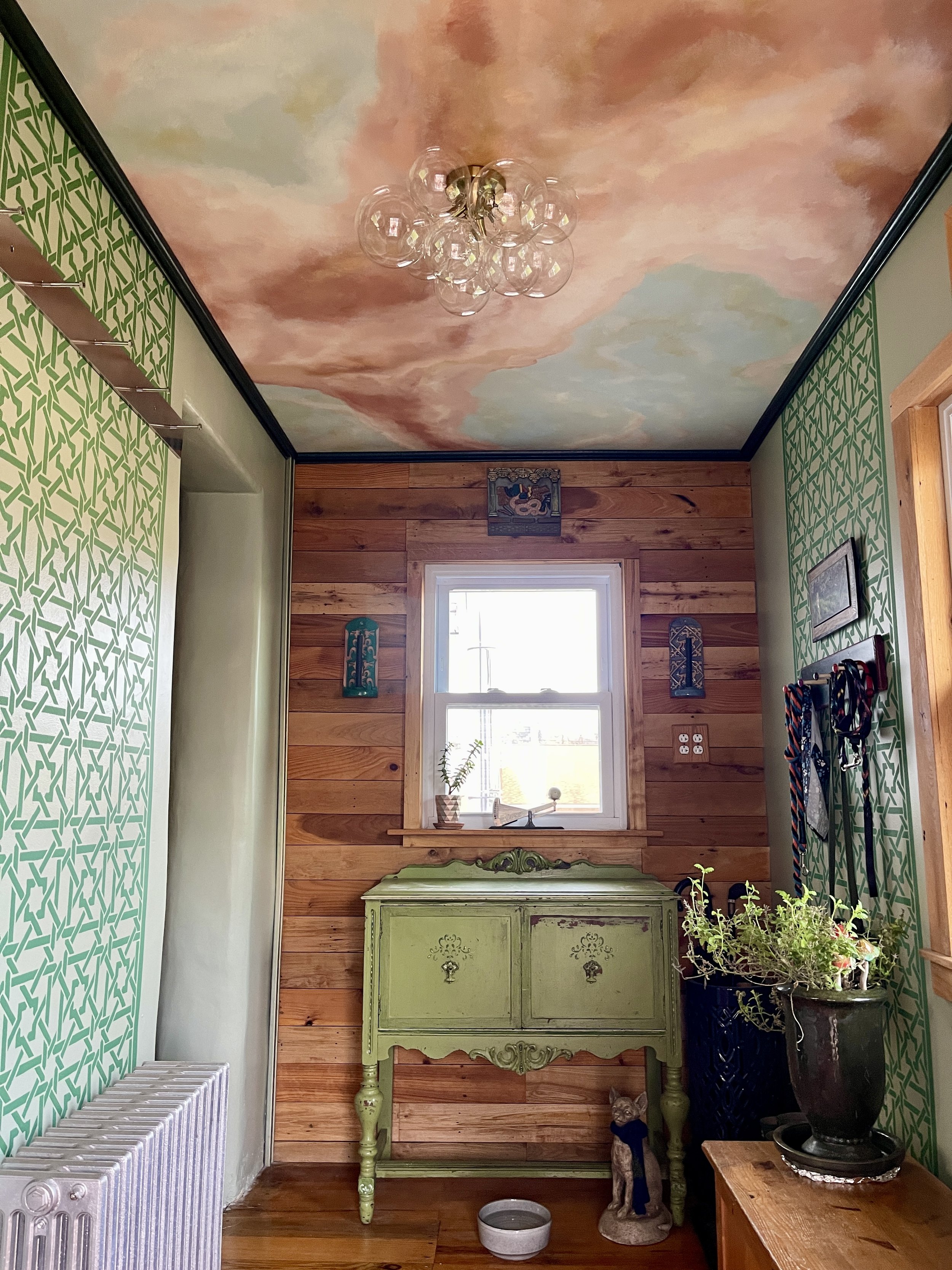 Faux finished mud room featuring a view of the swirling sunset clouds painted ceiling, along with stenciled green trellis walls.  In the background are Moravian Tile candle sconces and Mercer mosaic tiles "Sea of Darkness", Designed and painted by ar