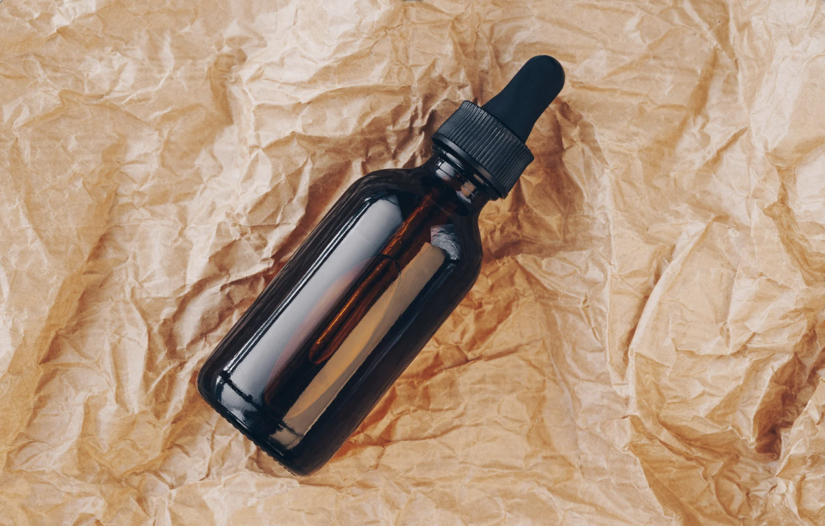 A dark amber glass dropper bottle with a black dropper cap, placed on crumpled brown paper.