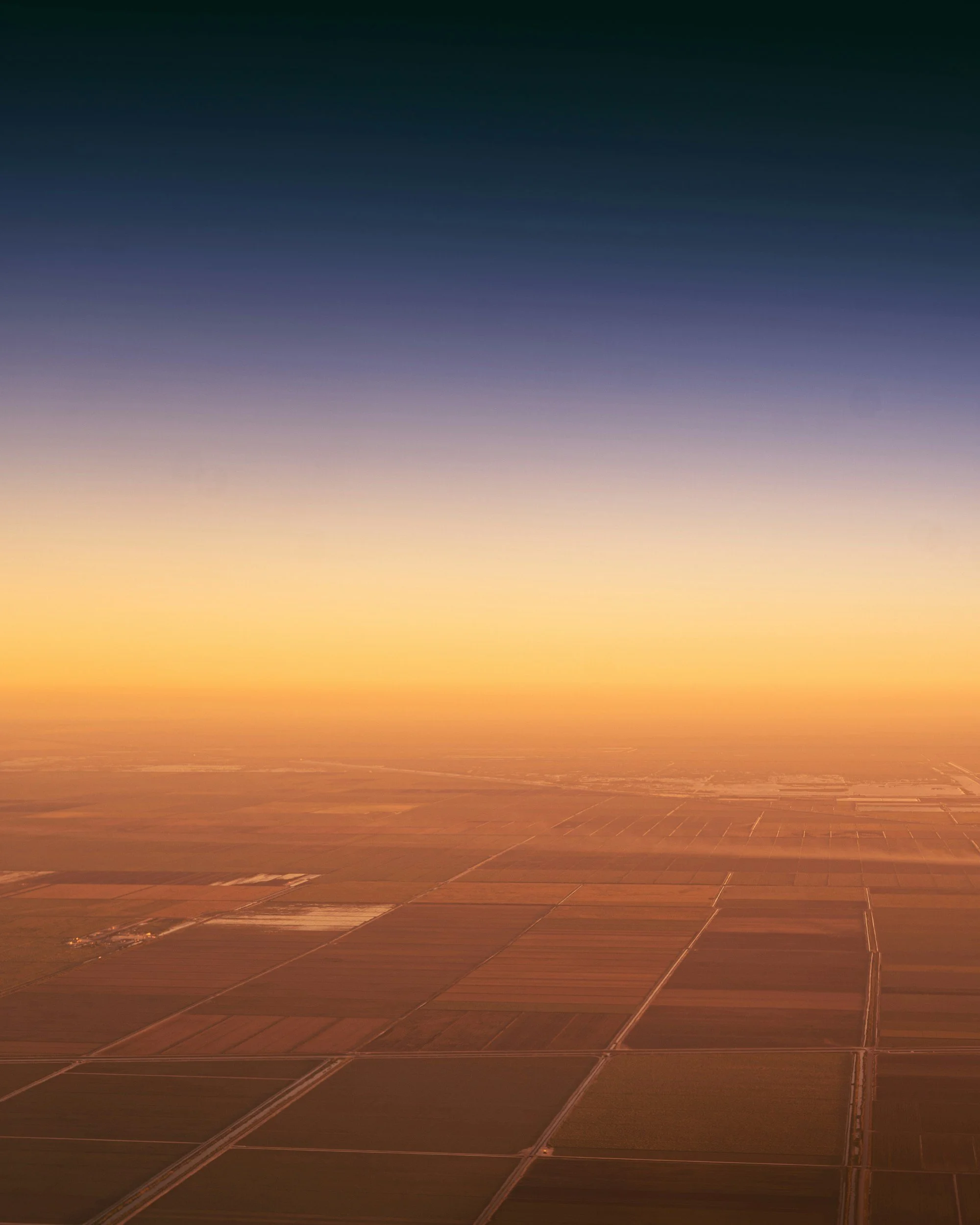 Aerial view of farmland at sunset with a colorful sky transitioning from orange to dark blue.