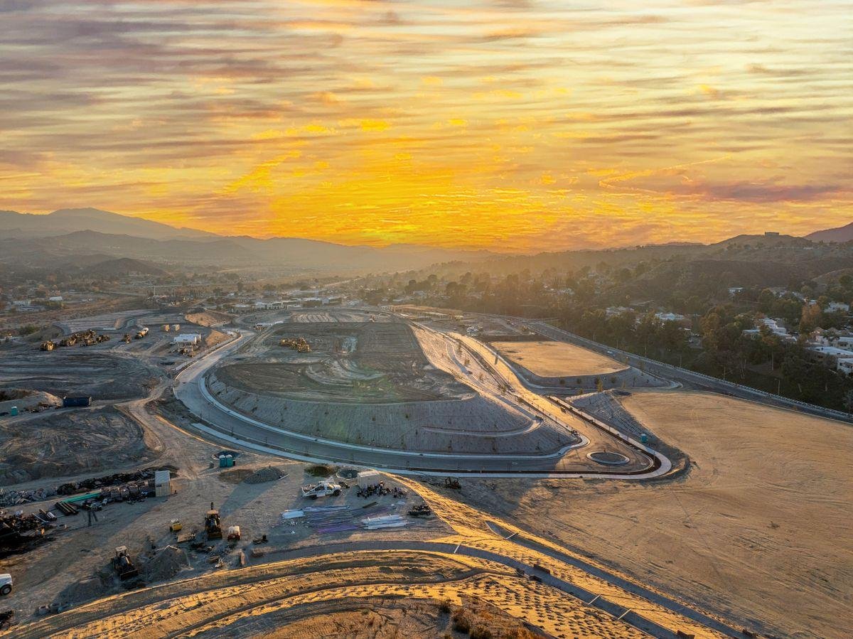 Large land and infrastructure development under construction with graded roads, hillside earthwork, and surrounding urban development.