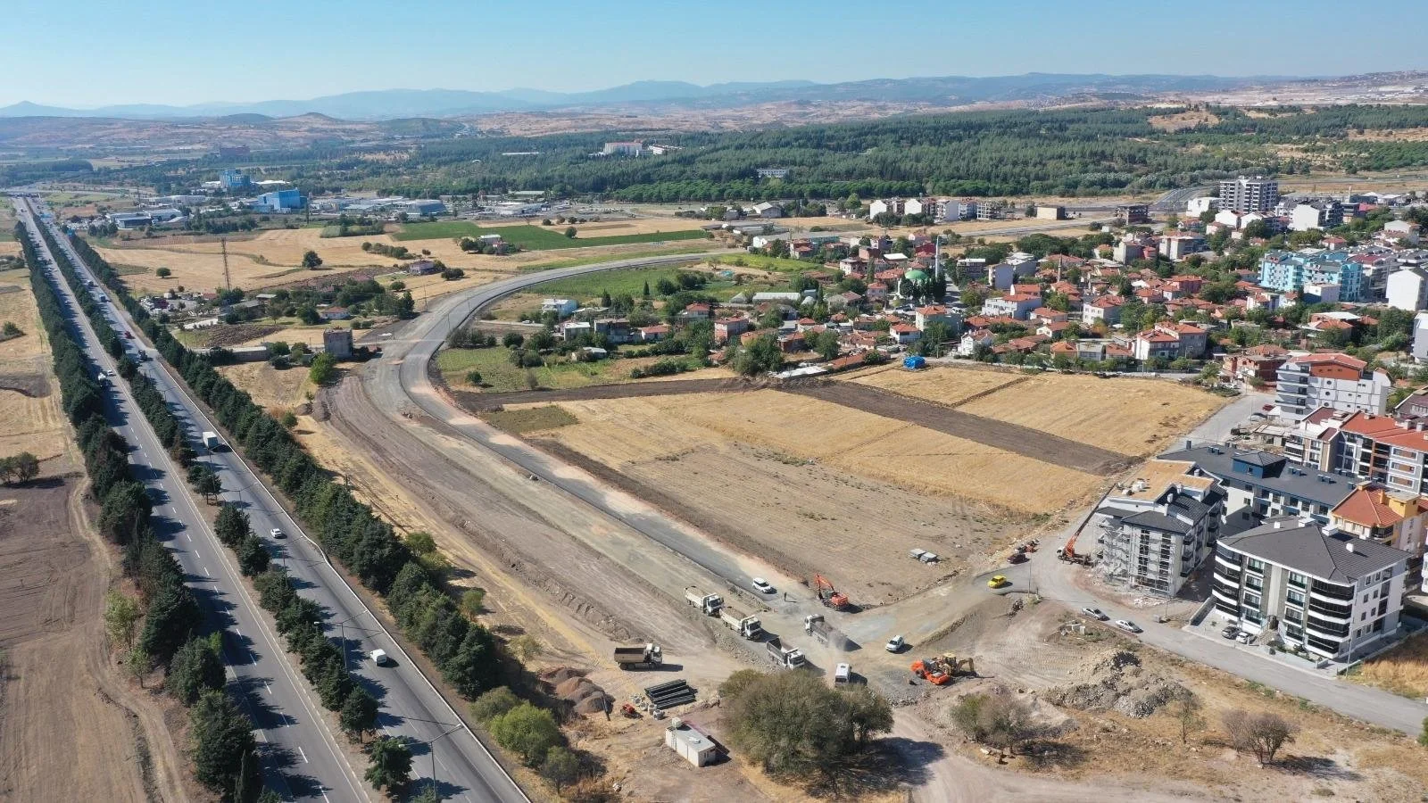 Active land development site with earthwork, construction equipment, building pads, and surrounding infrastructure.