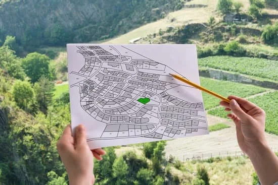 Person holding a map of a neighborhood with streets and a green area, outdoors with trees and hills in the background.