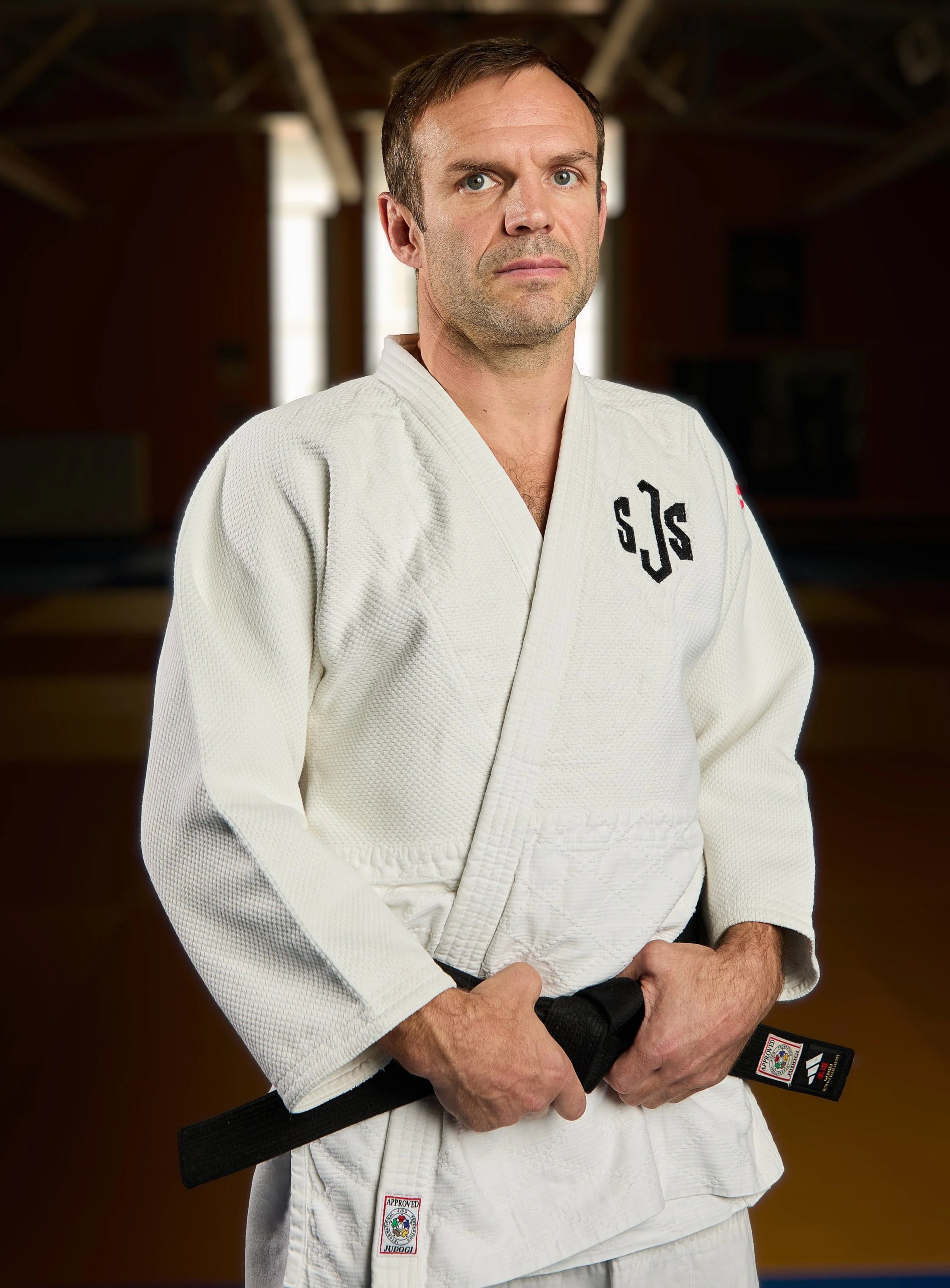 A man in a white martial arts gi standing against a black background.