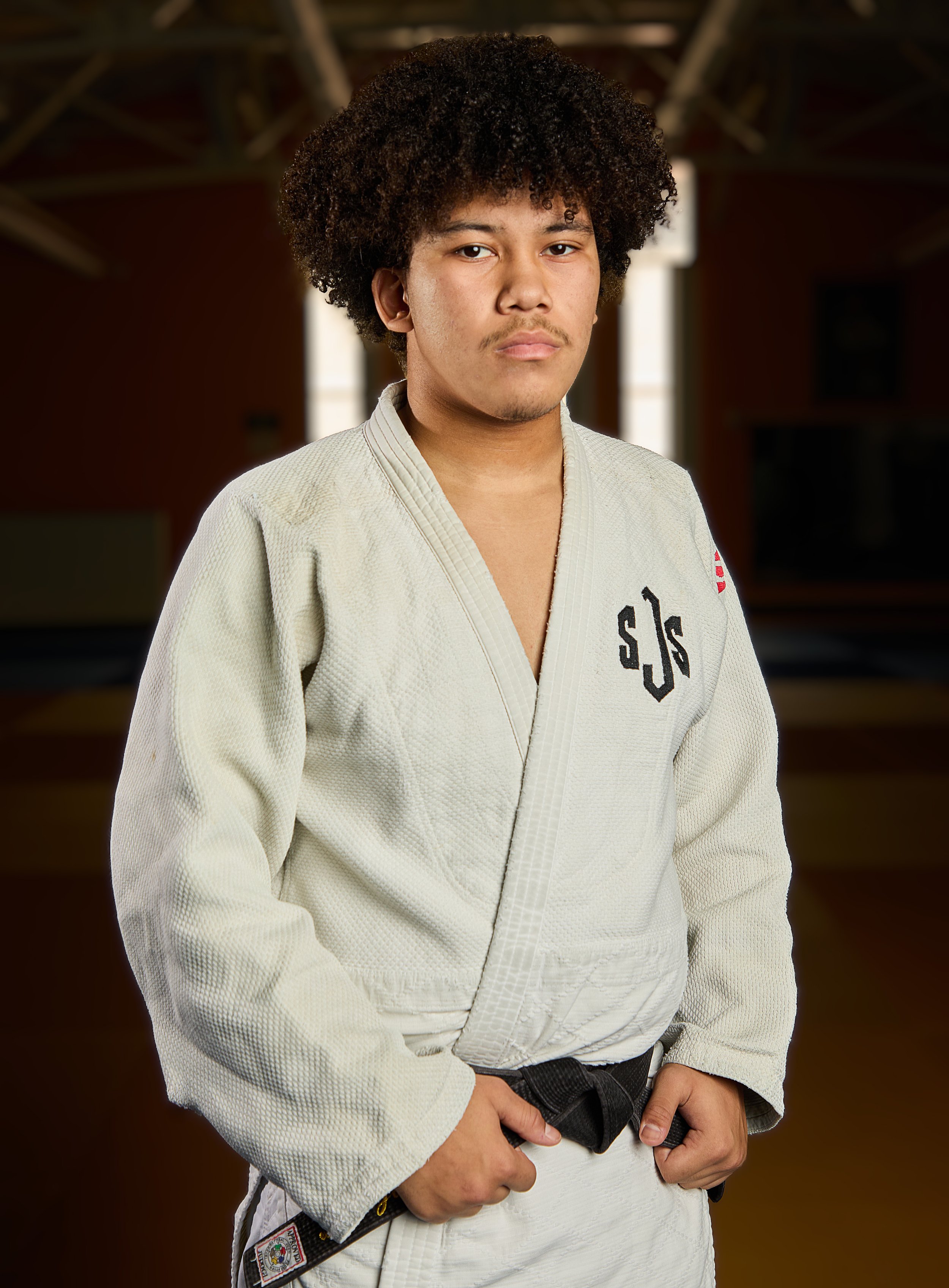 Weston Uyekawa. A young man in a white judo gi holding a black belt, standing against a black background, smiling at the camera.