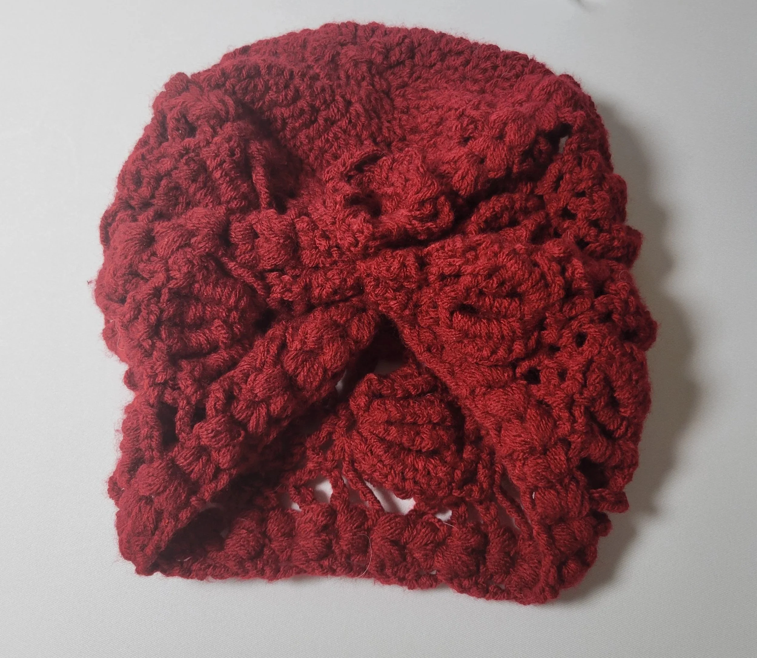 Red crocheted scarf or head wrap resting on a plain white surface.