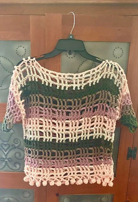 Colorful crocheted top hanging on a hanger against a wooden door.