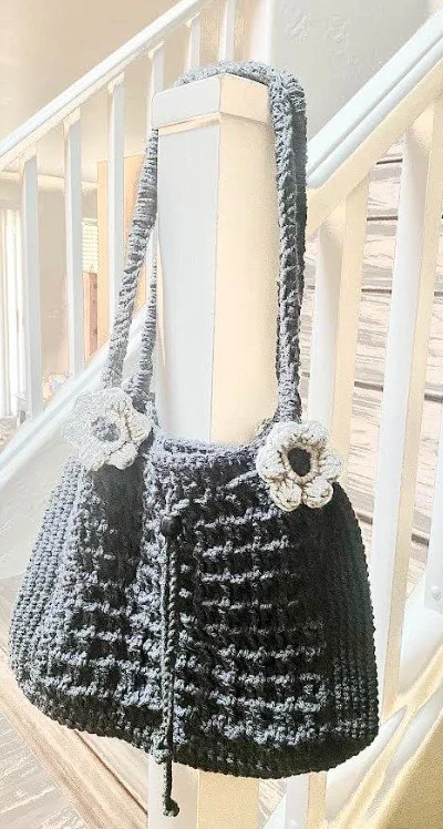 A black and white knitted handbag with floral decorations hanging on a staircase railing.
