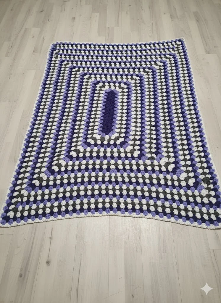 A colorful, circular crocheted rug with a purple, white, gray, and black pattern, placed on a light wooden floor.