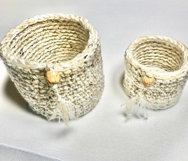 Two small, hand-crocheted baskets with a decorative button on each, placed on a white surface.