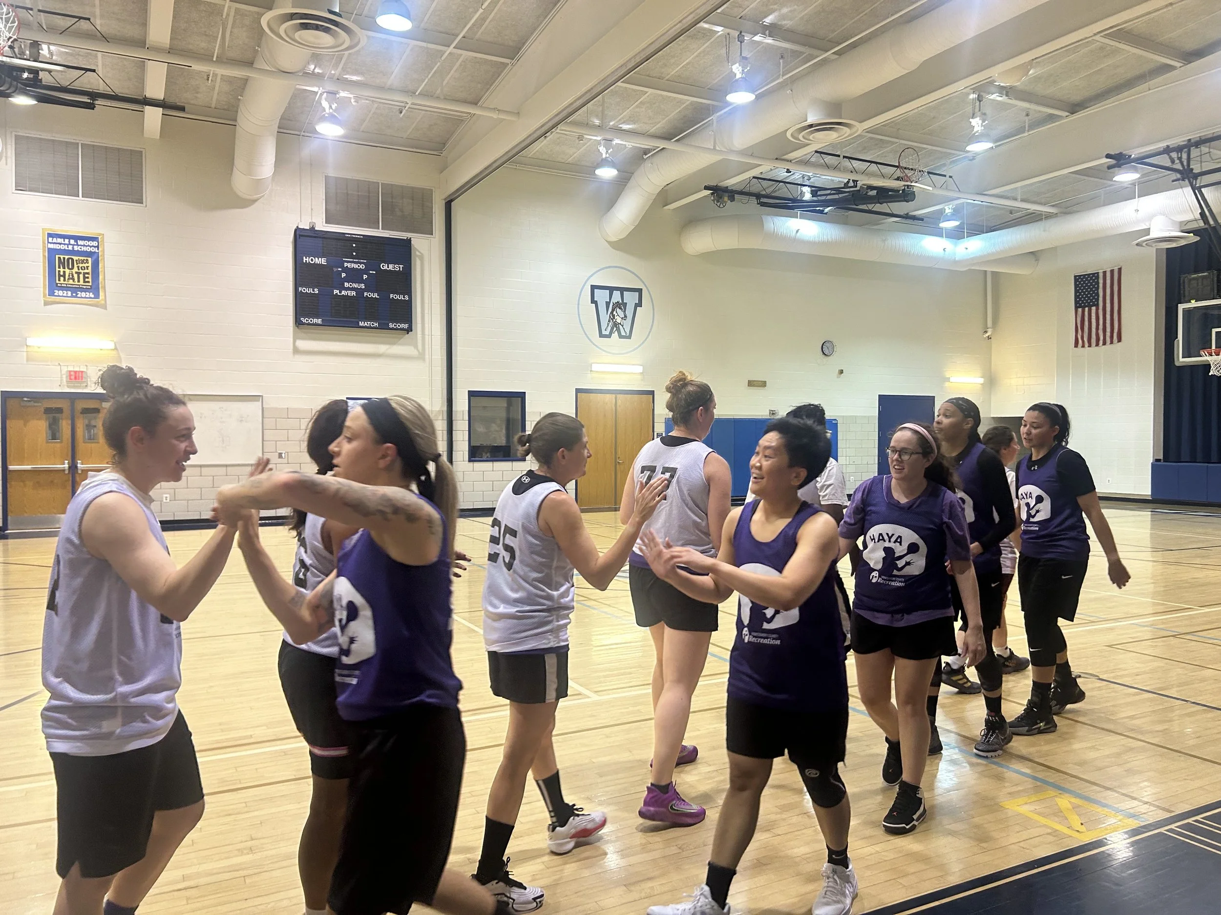 Two teams of basketball players are shaking hands in a gymnasium after a game.