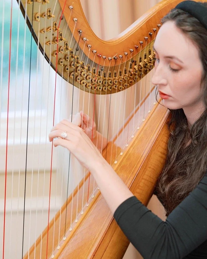 A woman playing a wooden harp, focusing on plucking the strings with her right hand.