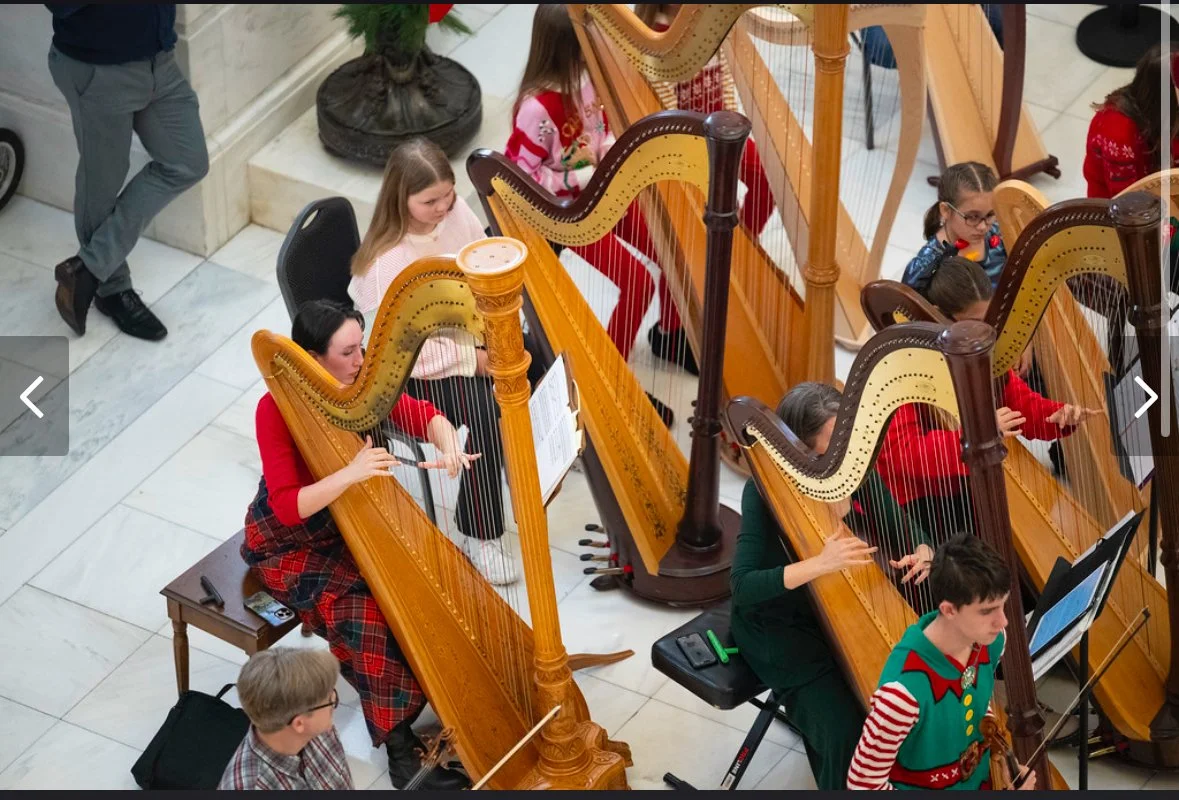 Children playing harps at a concert or musical performance in a public indoor space.