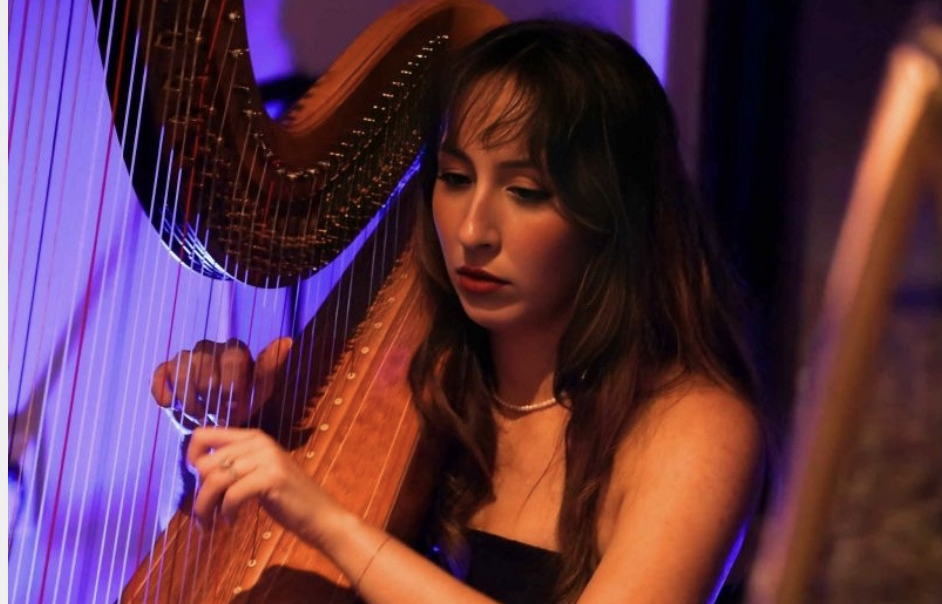 A woman playing a harp in a dimly lit room with purple and orange lighting.