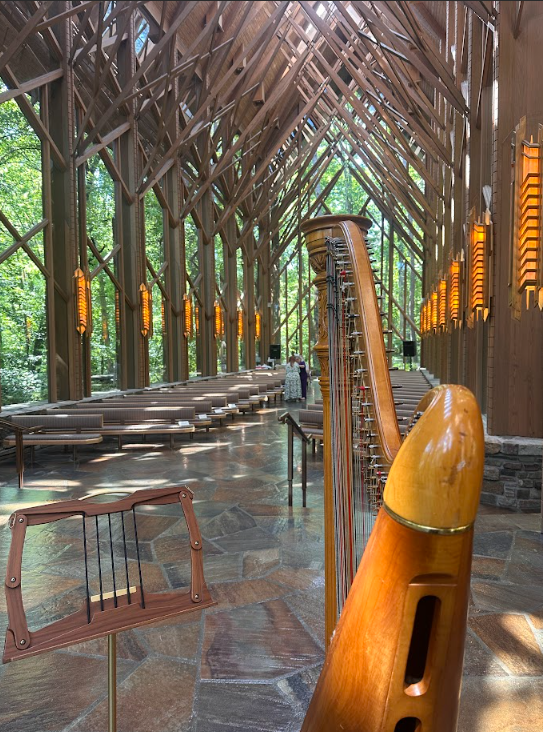Inside a modern wooden church with tall, intricate wooden beams, orange light fixtures, and a harp in the foreground.