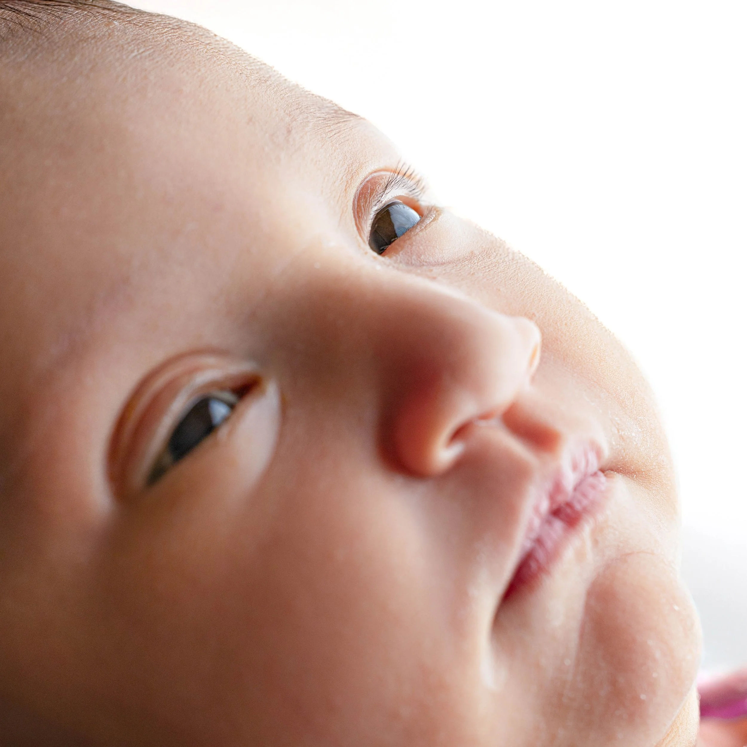 Close-up of a baby's face showing both eyes and part of the nose with skin details, soft natural lighting, minimal background.