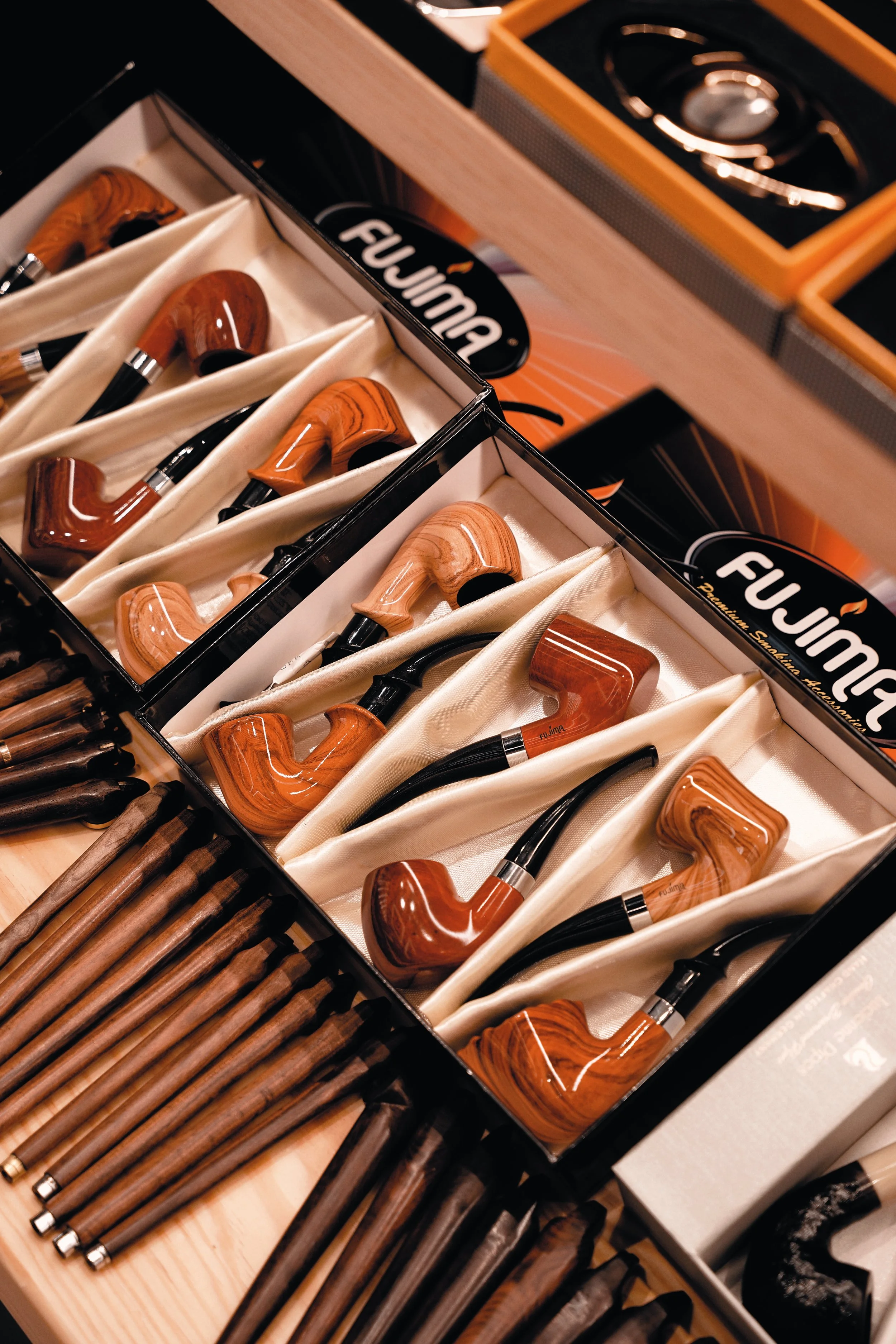 A display of wooden smoking pipes in boxes, with additional wooden smoking pipes and other smoking accessories on a wooden surface, all arranged for sale.