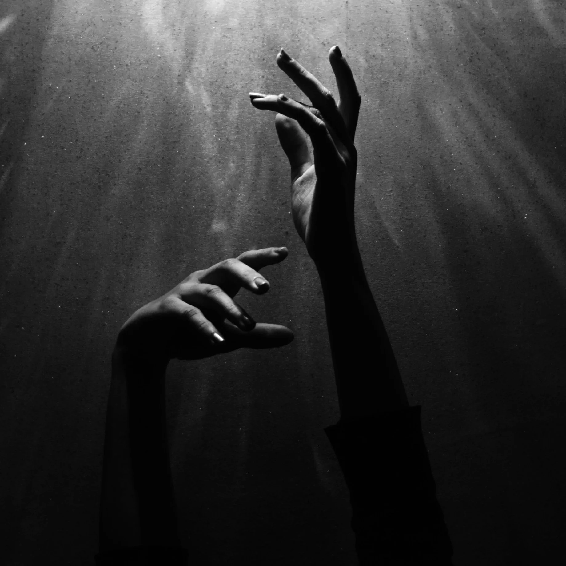 Black and white photograph of two hands with extended fingers reaching toward a textured surface, illuminated by light rays from above.
