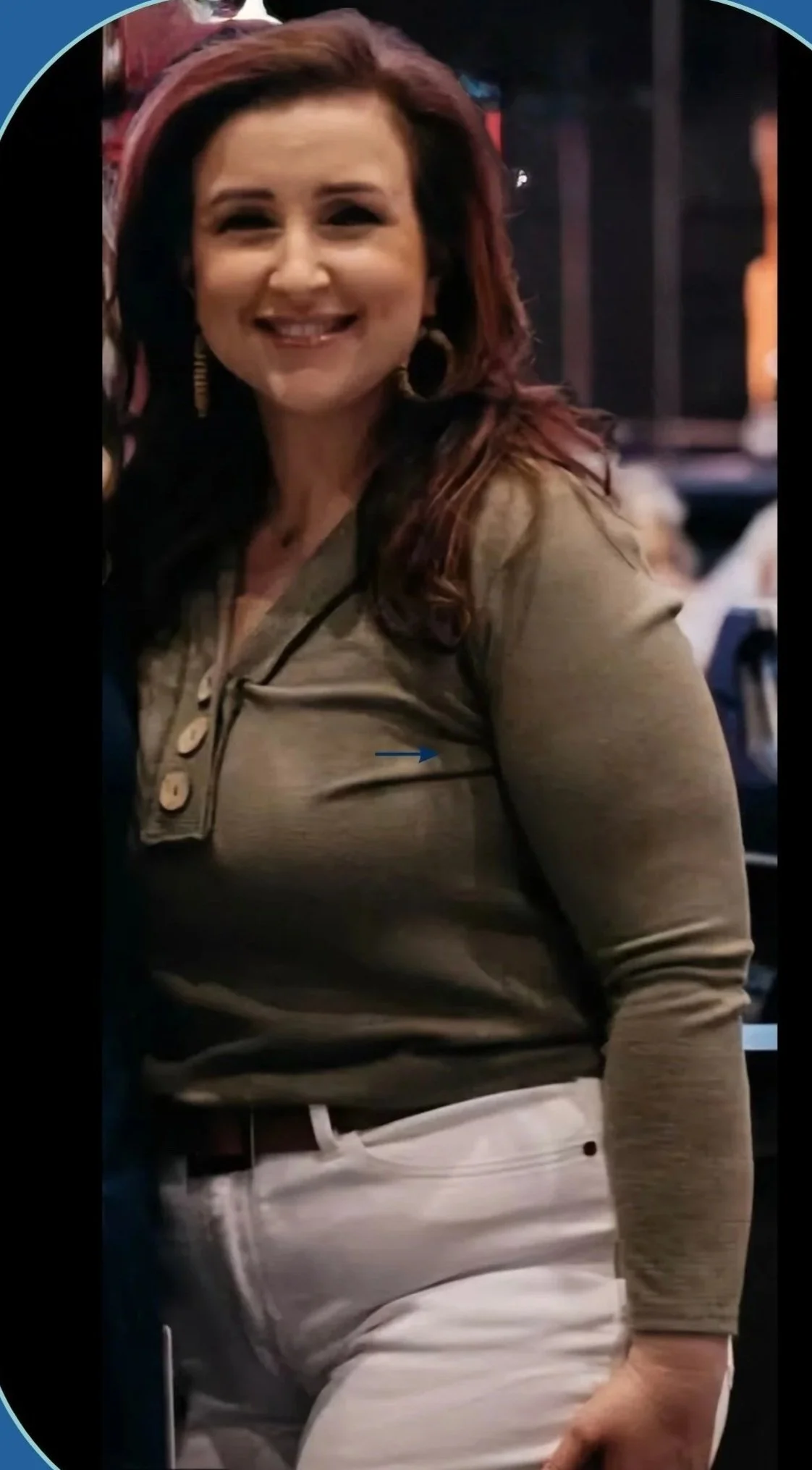 A woman with shoulder-length, reddish-brown hair, wearing a khaki long-sleeve shirt and white pants, smiling and posing indoors.