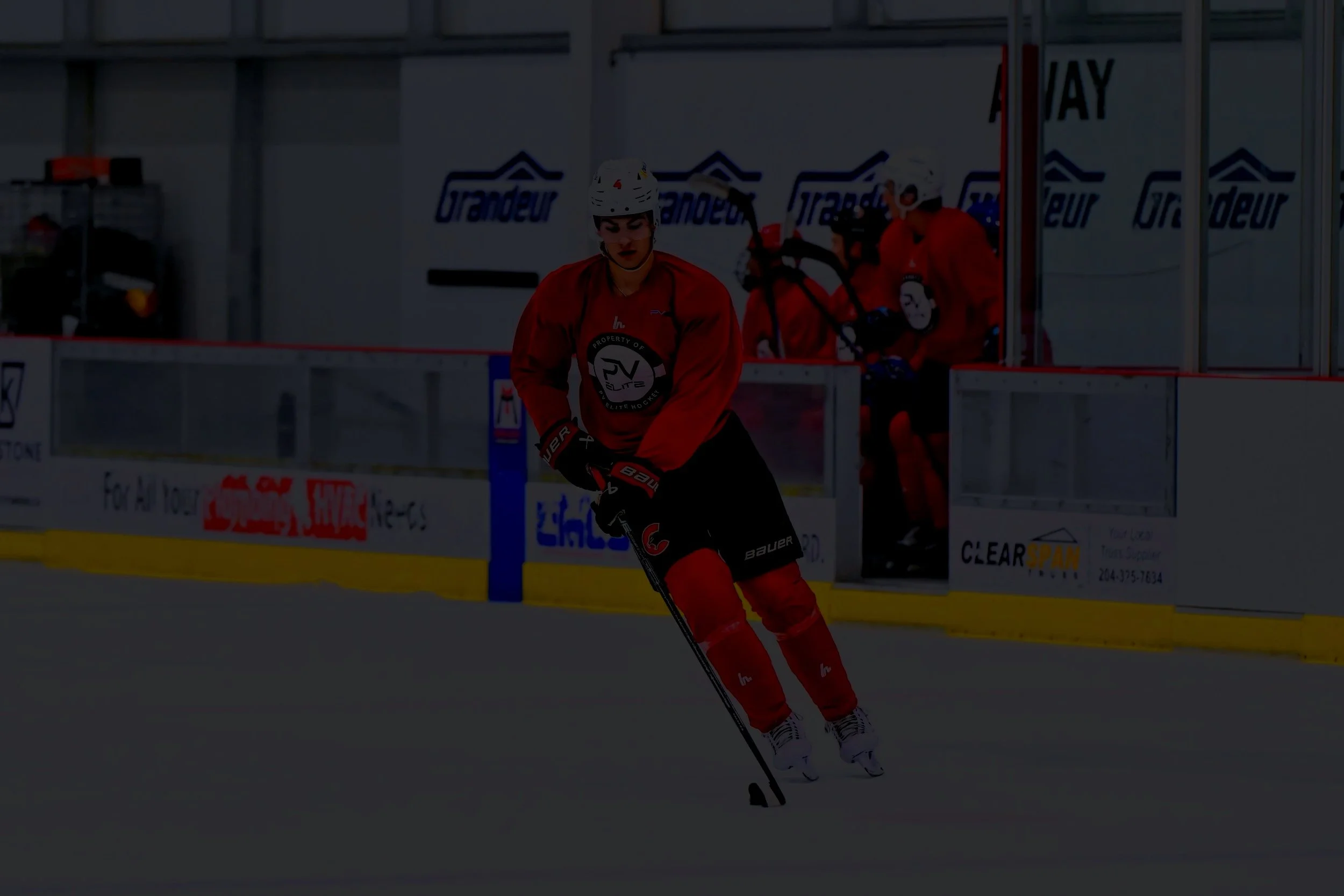 A hockey goalie in white and blue gear is on the ice, ready to make a save, with a black puck in midair near the net. Goaltending Development PV Elite Hockey.