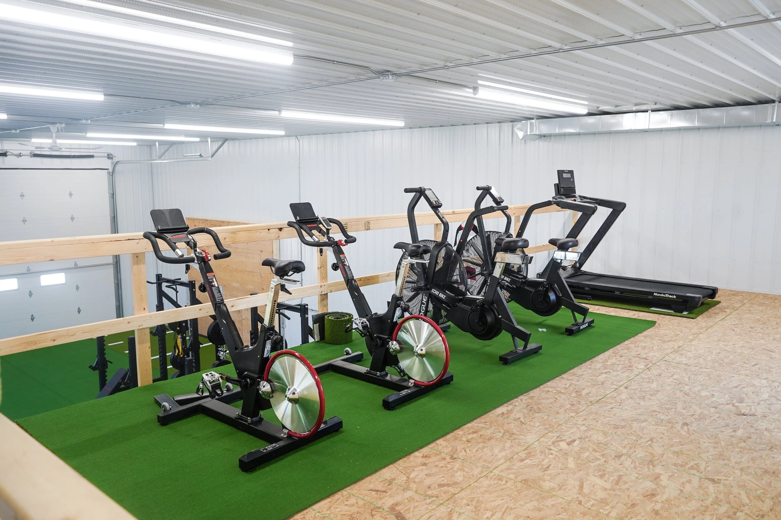 Indoor gym area with exercise bikes, a treadmill, and a rowing machine on green turf flooring. Off-season hockey training, Hockey development, training, PV Elite Hockey, Mitch Dyck Performance Centre