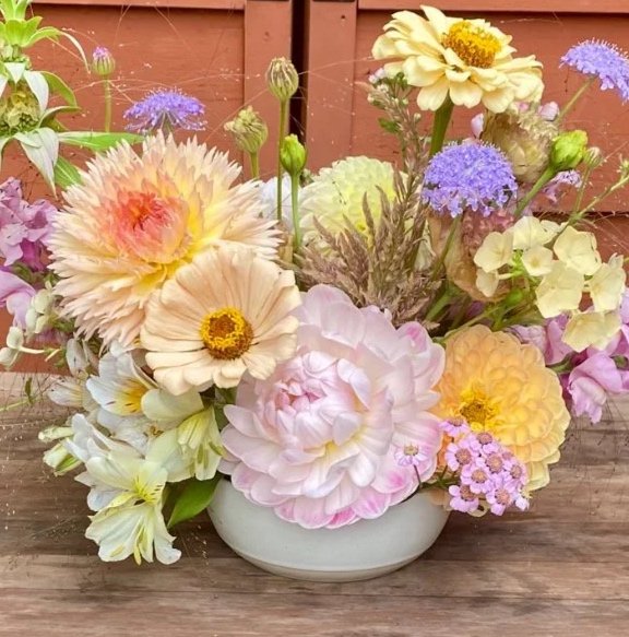 A bouquet of various colorful flowers in a white vase outdoors, with a wooden fence in the background.