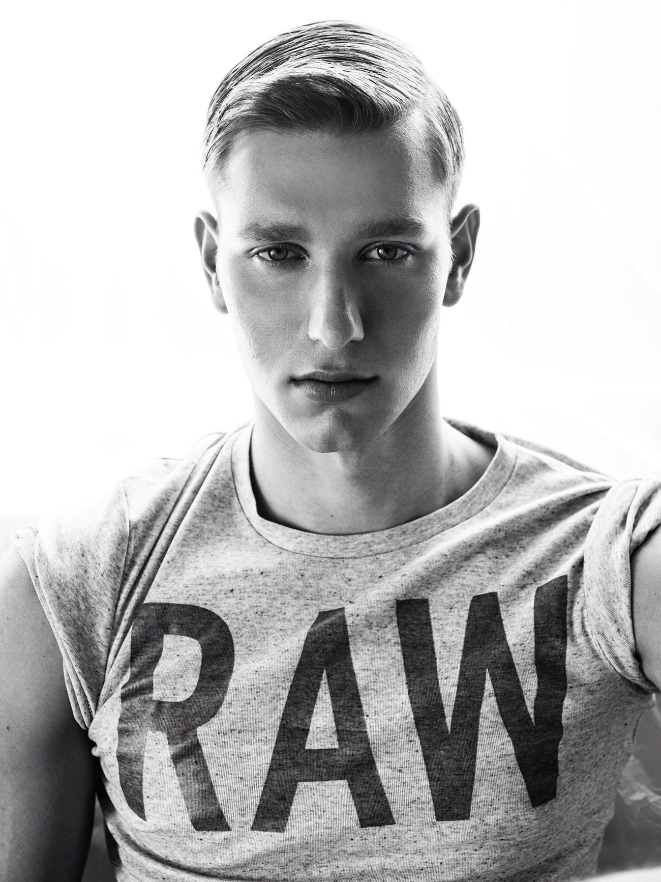 Black and white photo of a young person with short, styled hair, wearing a T-shirt with the word 'RAW' printed on it.