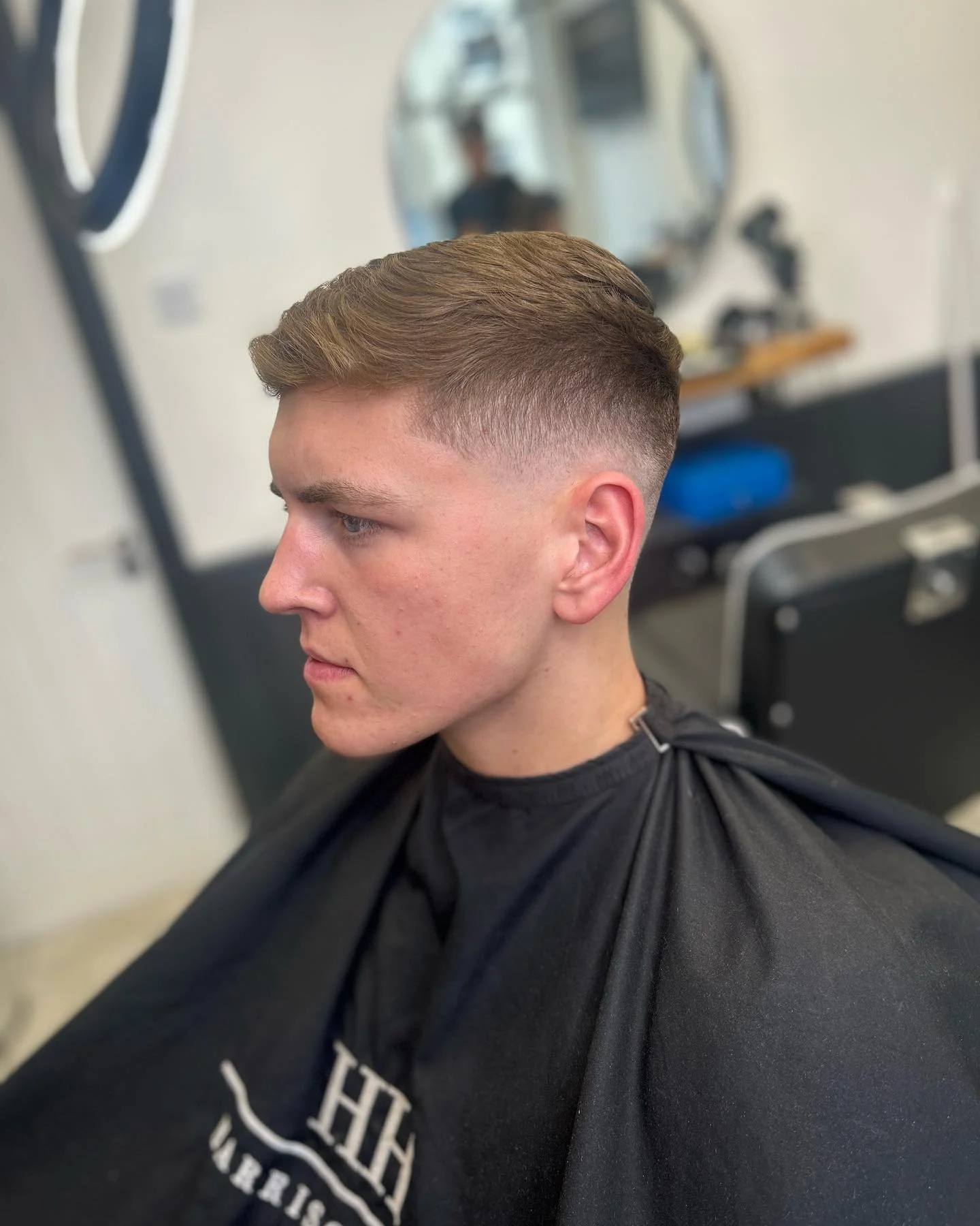 Young man with a short, faded haircut sitting in a barbershop chair.
