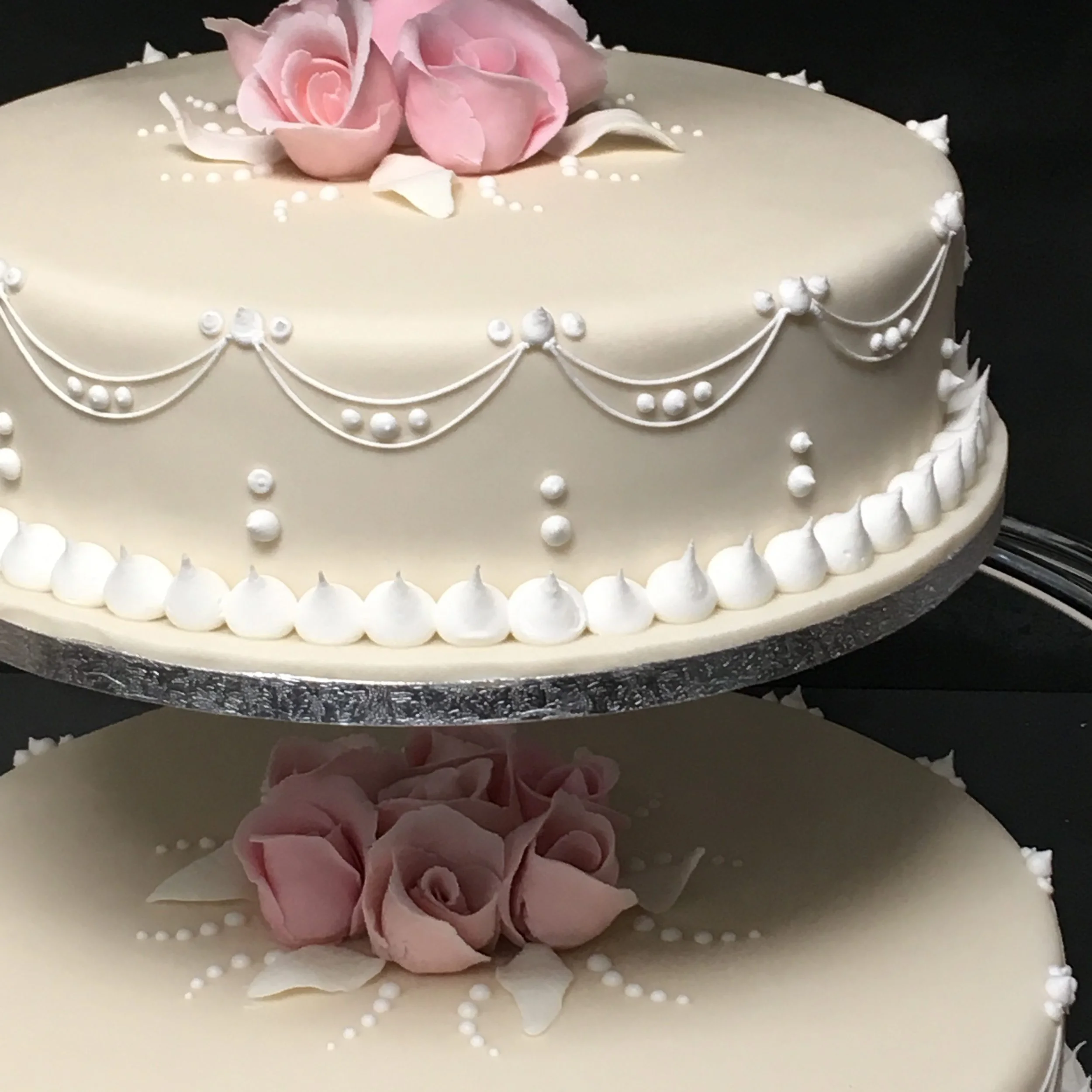A white round wedding cake decorated with pink roses on top, white piped frosting details, and pearl-like edible decorations.