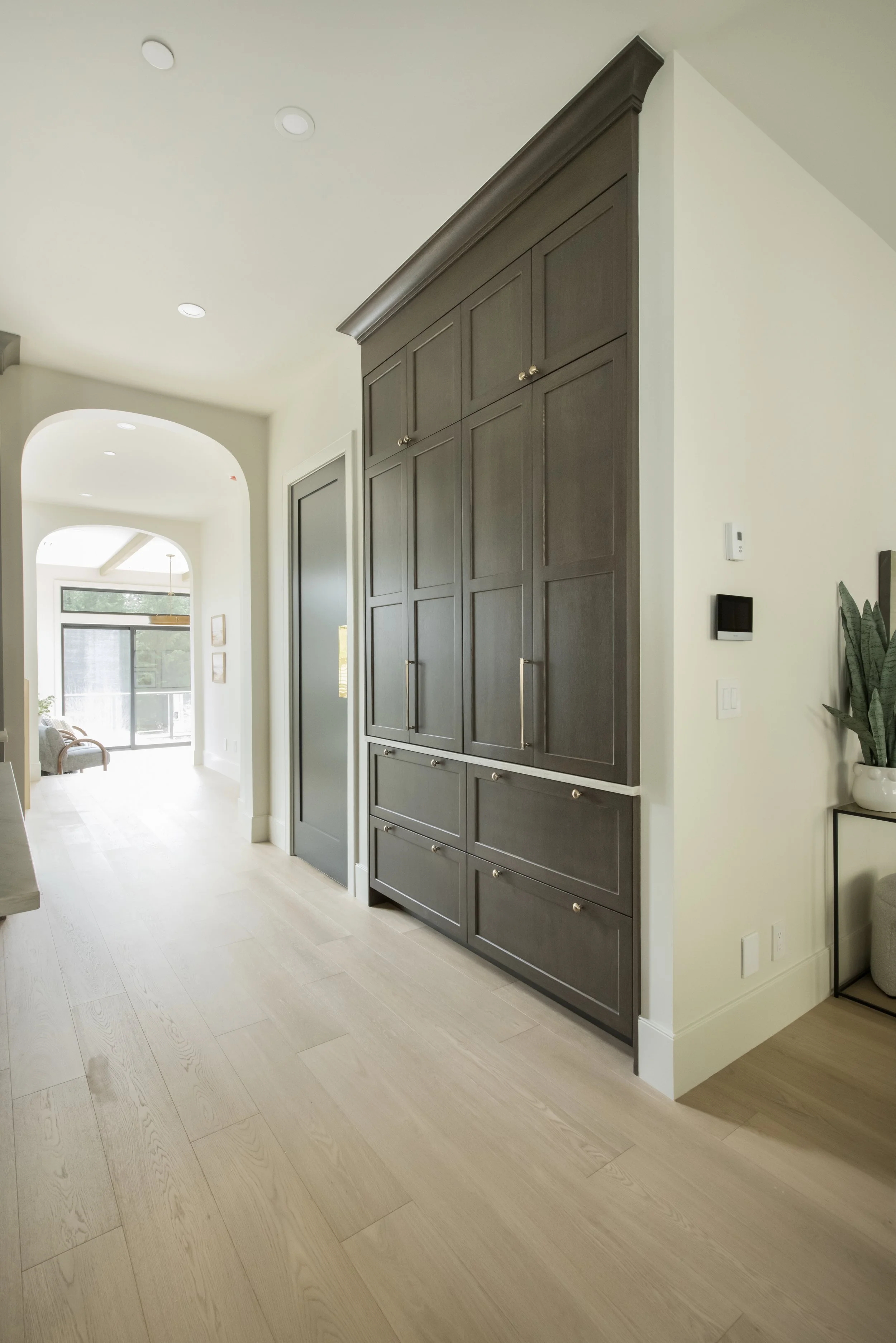 Interior view of a modern home hallway with light wood flooring and a large dark wood built-in cabinet.