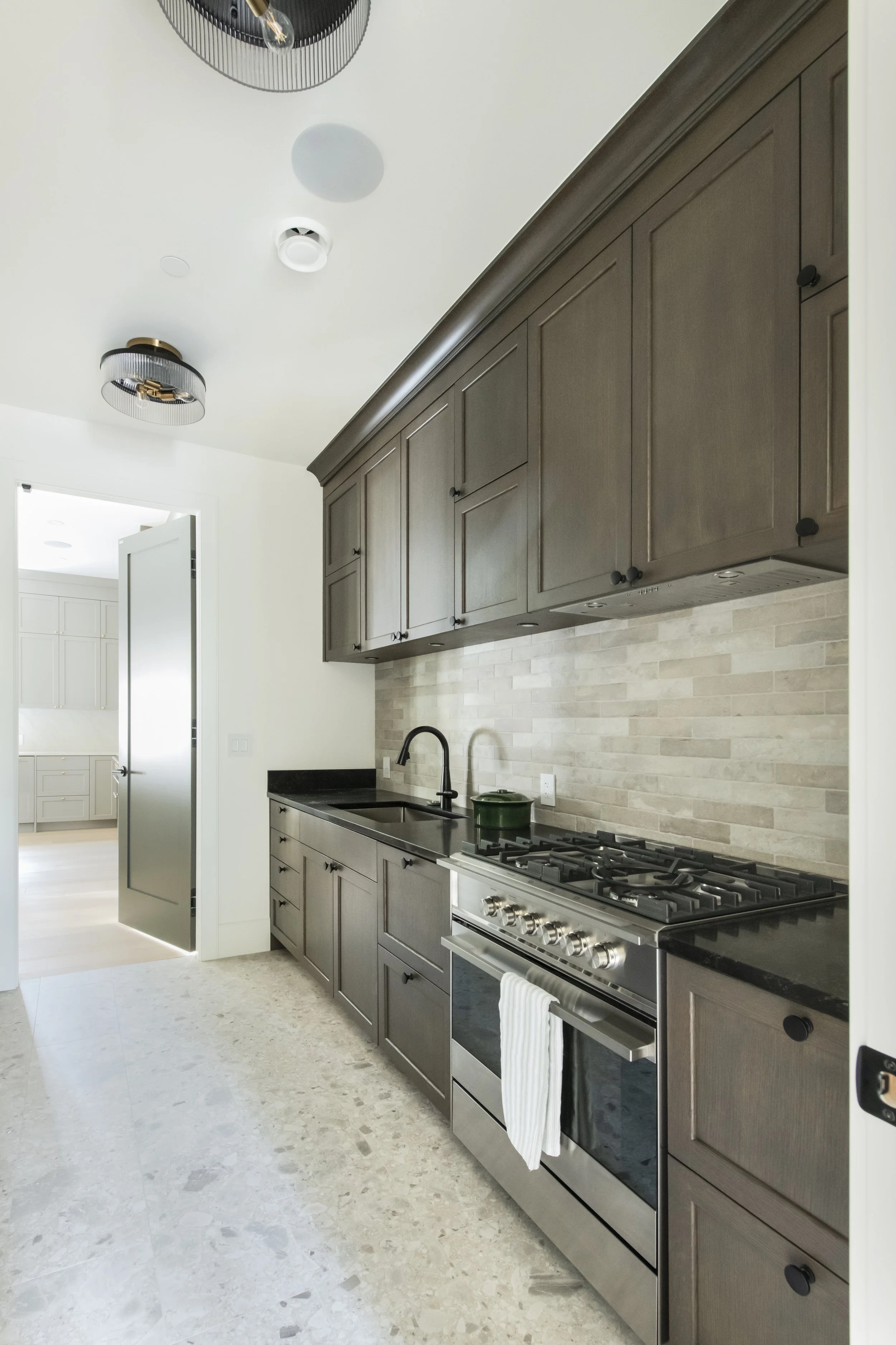 Kitchen with dark wood cabinets, a black countertop, beige tile backsplash, stainless steel oven, black faucet, and light-colored terrazzo flooring.