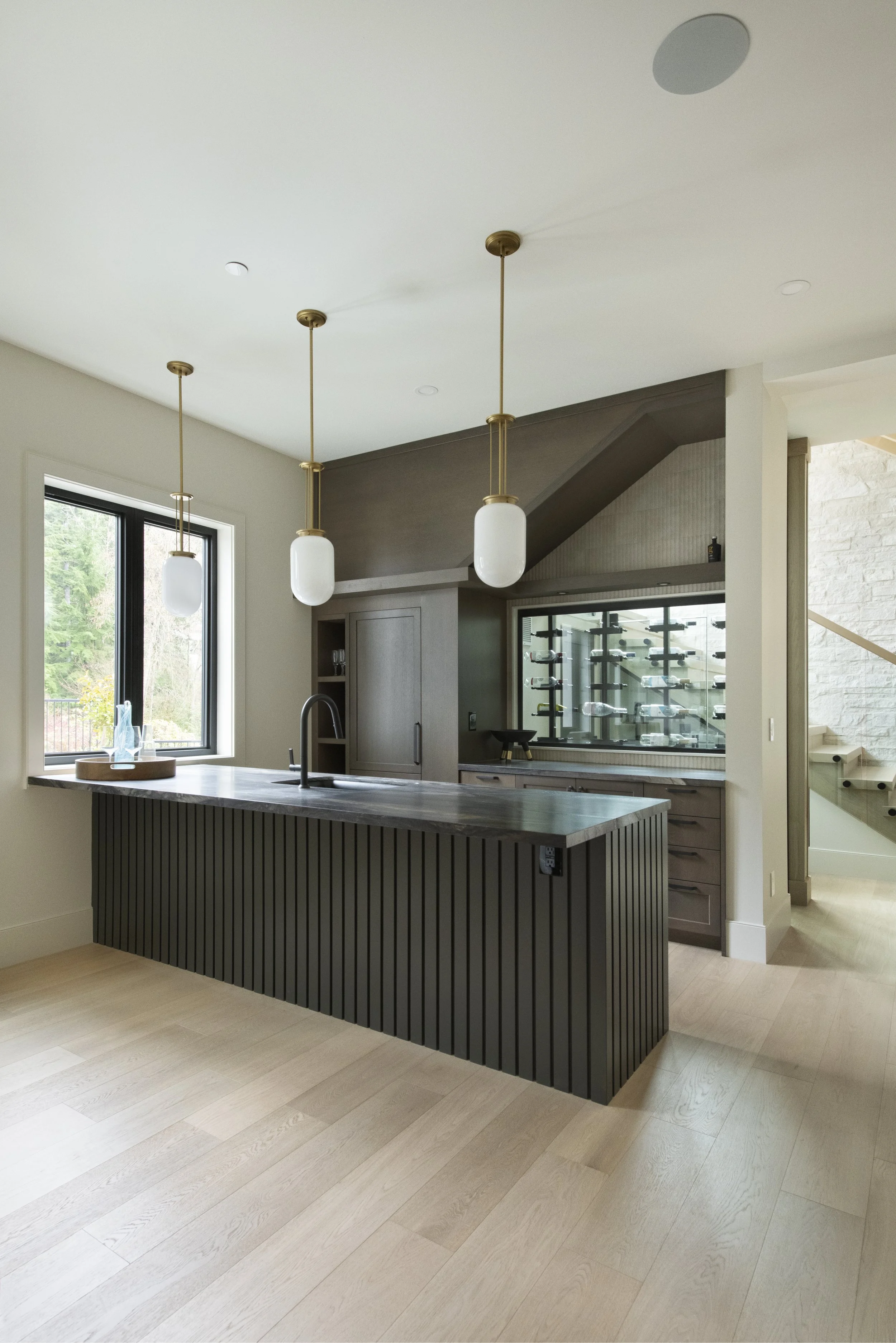 Modern kitchen with a black island, pendant lights, and a wine display in the background.