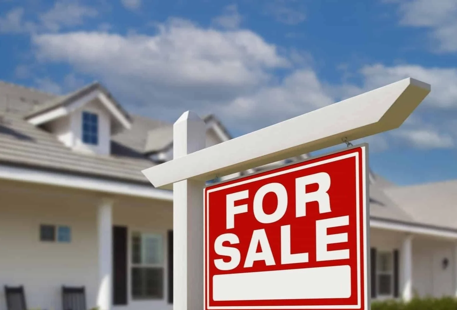 A white and red for sale sign in front of a house with a cloudy blue sky.
