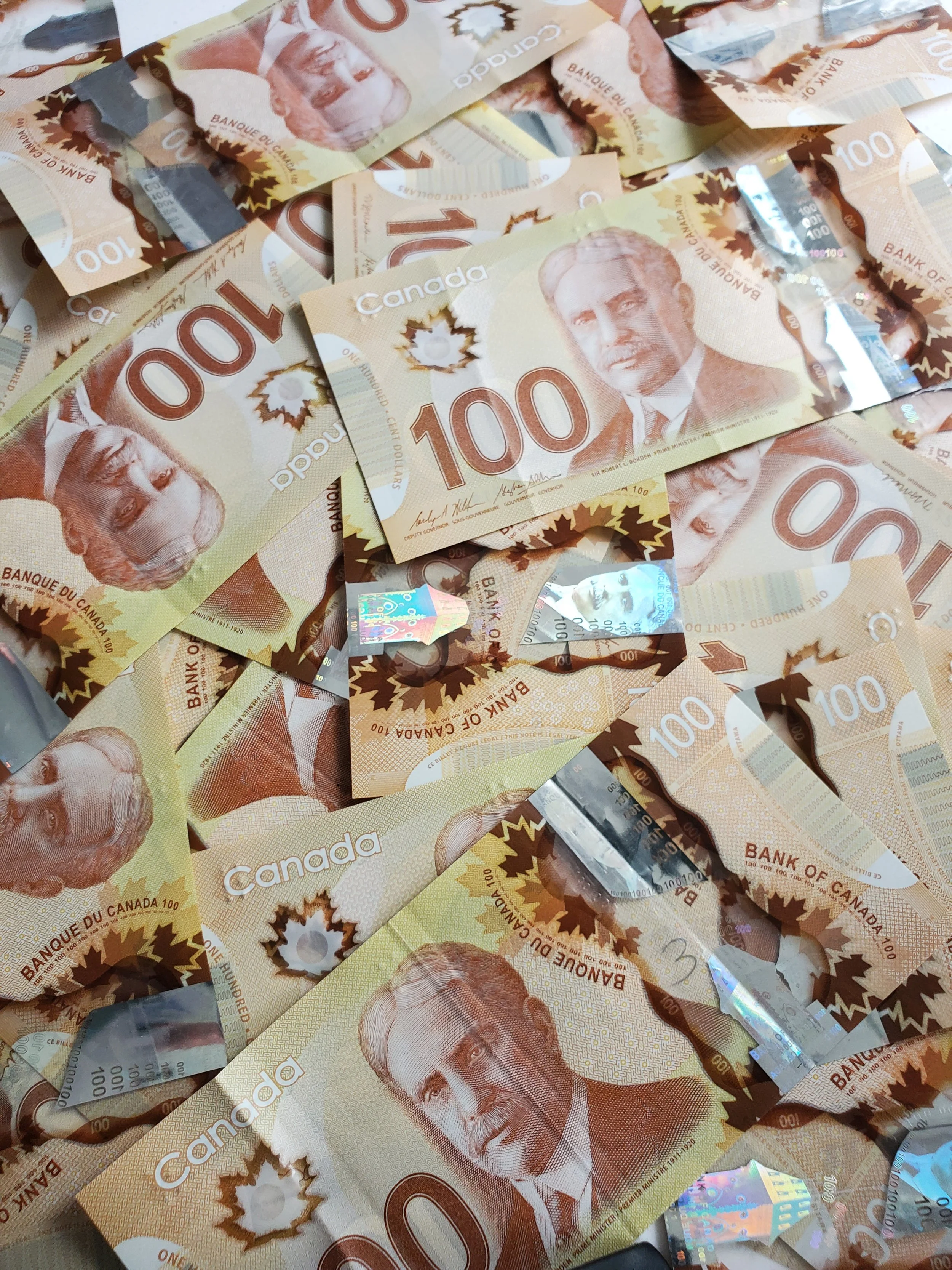 Numerous Canadian one hundred dollar bills scattered together.