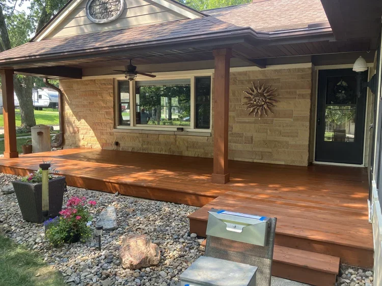 Back porch of a house with a wooden deck, stone landscaping, a flower pot, and outdoor furniture.