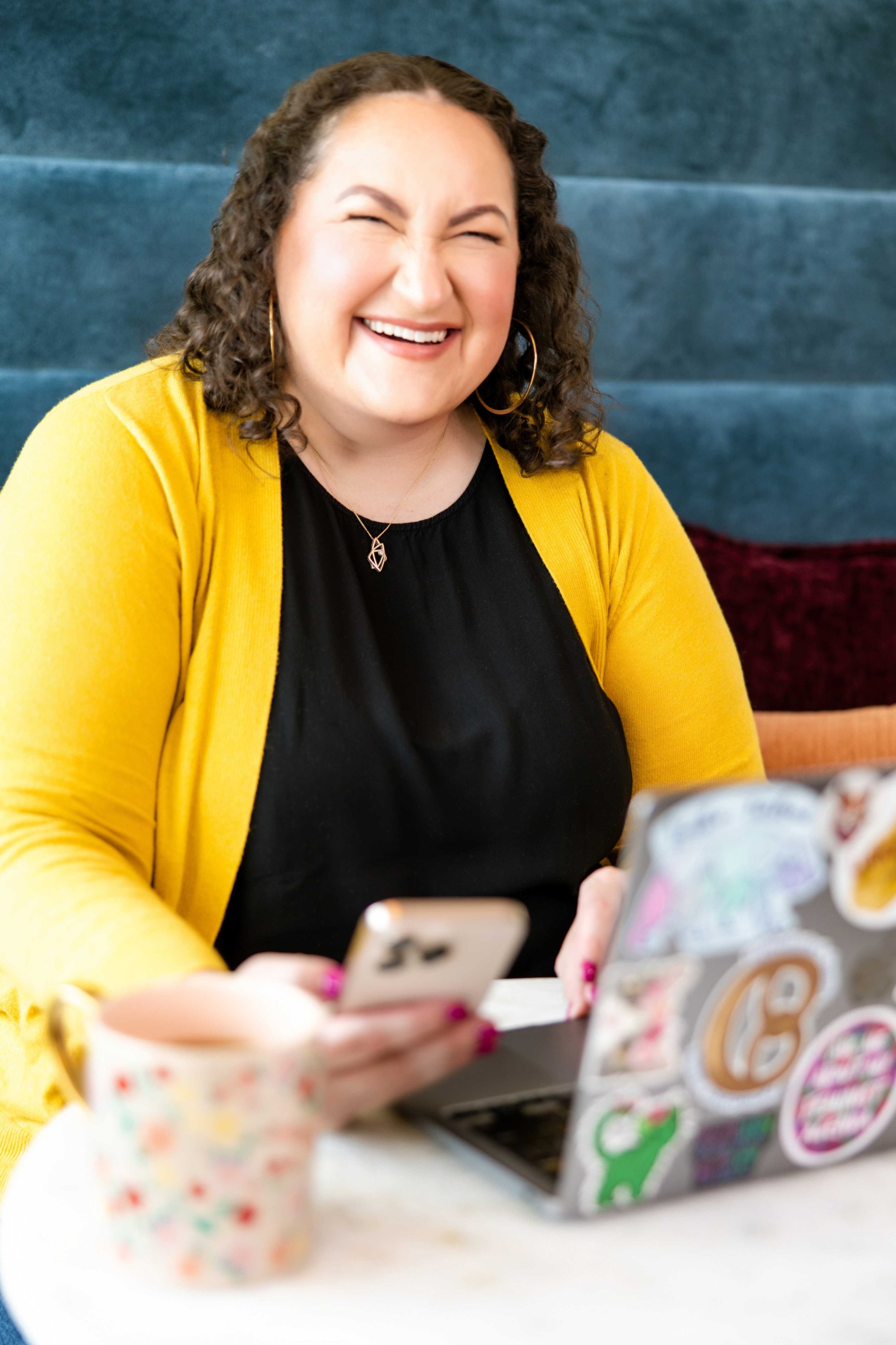 Golden Poppy Digital Owner Tori sitting at a table, smiling at the camera, with a mobile phone and a laptop.