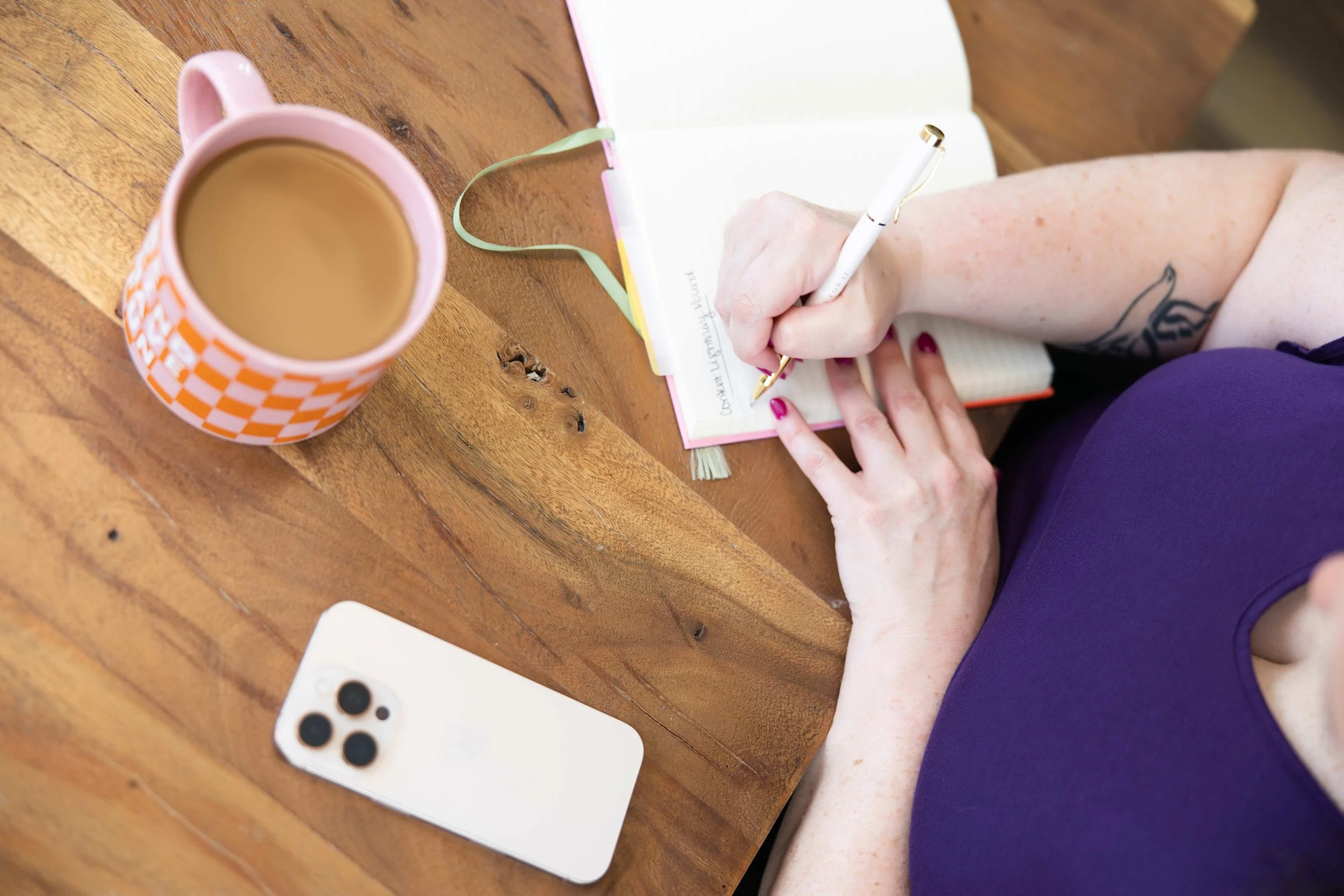 Golden Poppy Digital Owner Tori sitting at a table, writing in a notebook. Also on the table is a mobile phone.