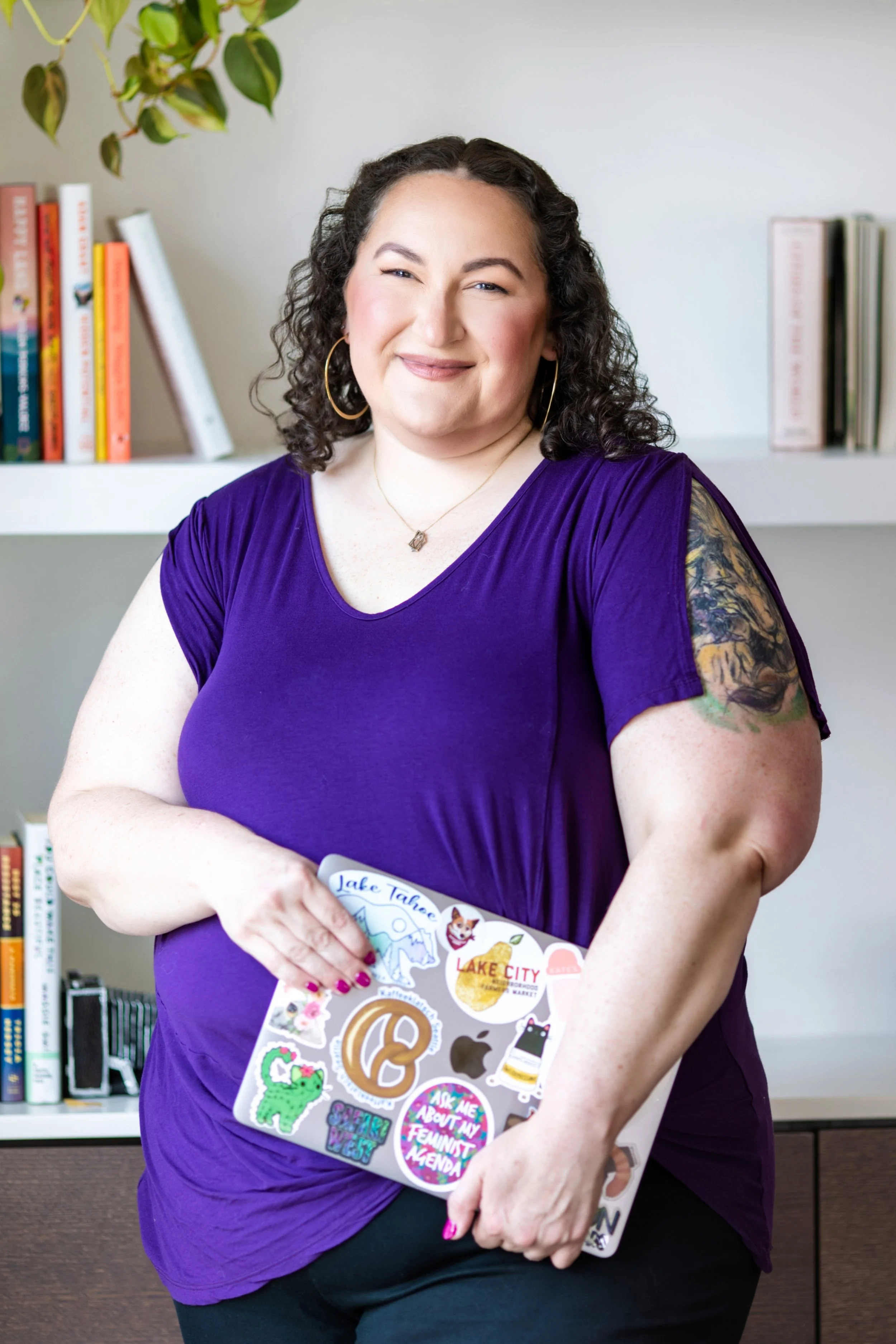 Golden Poppy Digital Owner Tori wearing a purple shirt, holding a laptop, in front of a bookshelf.