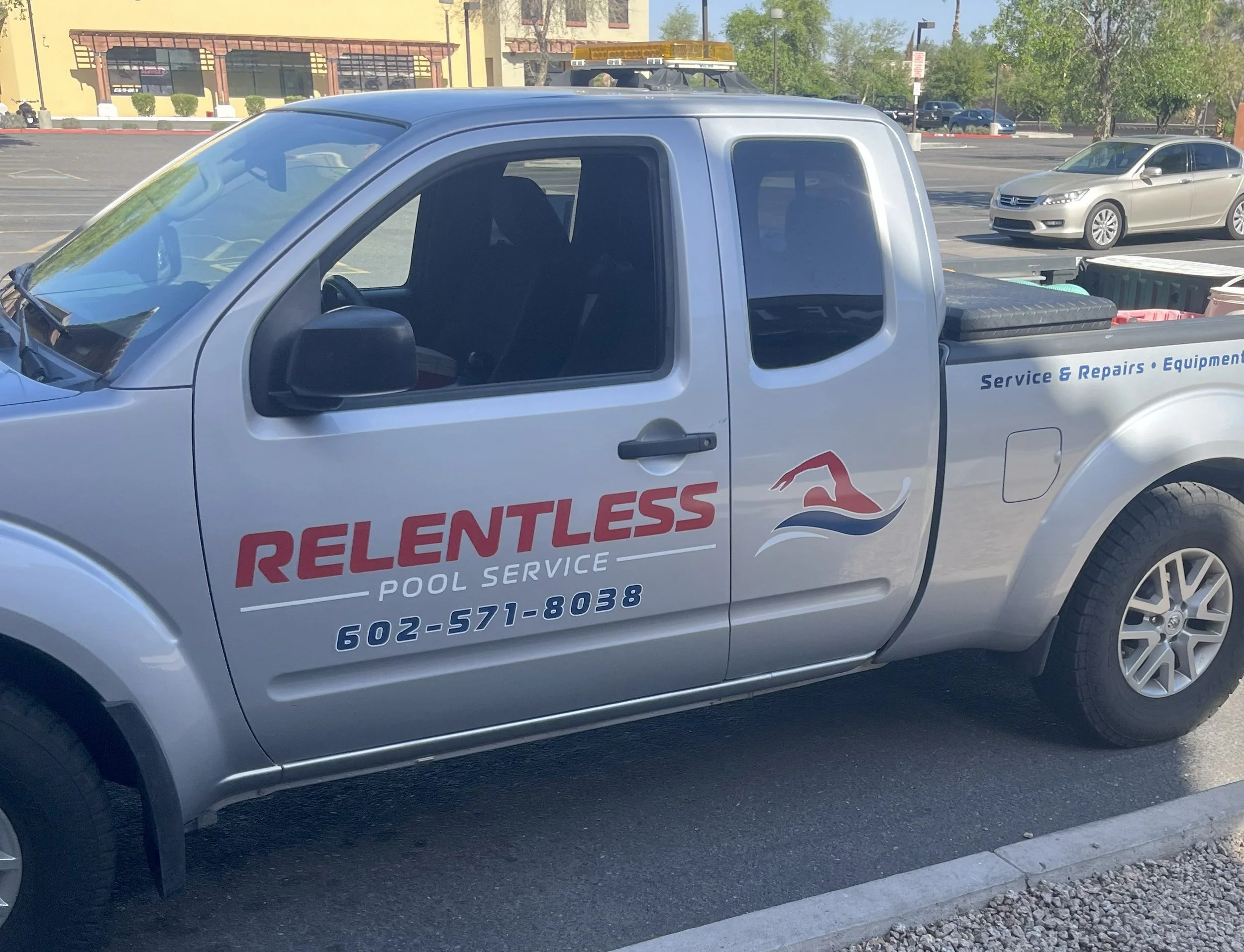 Silver pickup truck with red and blue lettering and logo for Relentless Pool Service, parked in a parking lot.