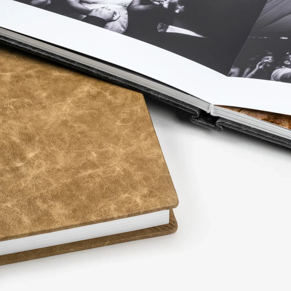 Duas plataformas de livros, uma com capa de couro marrom e outra com capa preta, uma das plataformas com uma revista com fotos em preto e branco e a outra apenas com páginas brancas visíveis.