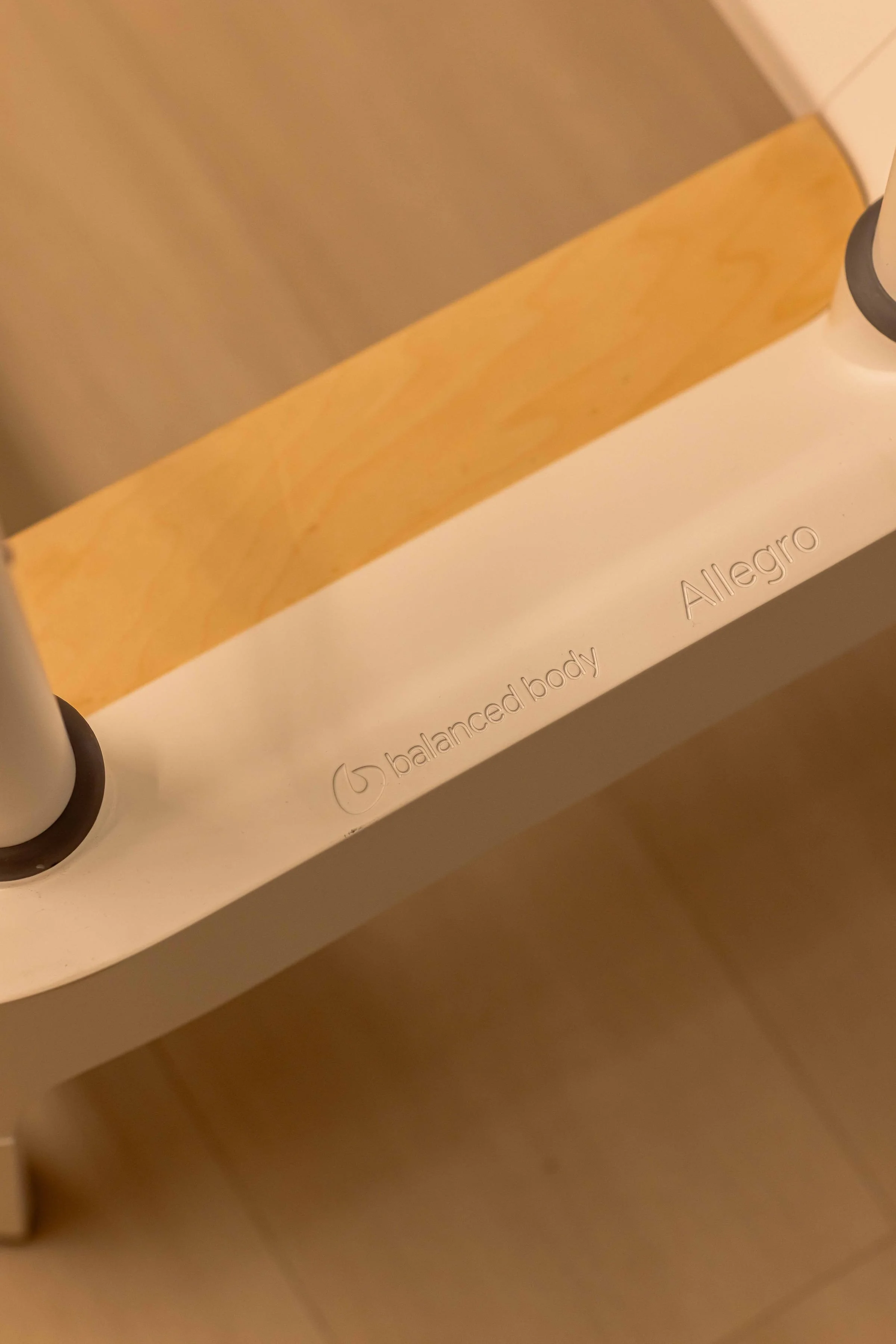 Close-up of a white standing paddleboard with the brands 'balanced body' and 'Allegro' inscribed on it, secured with black hand straps.