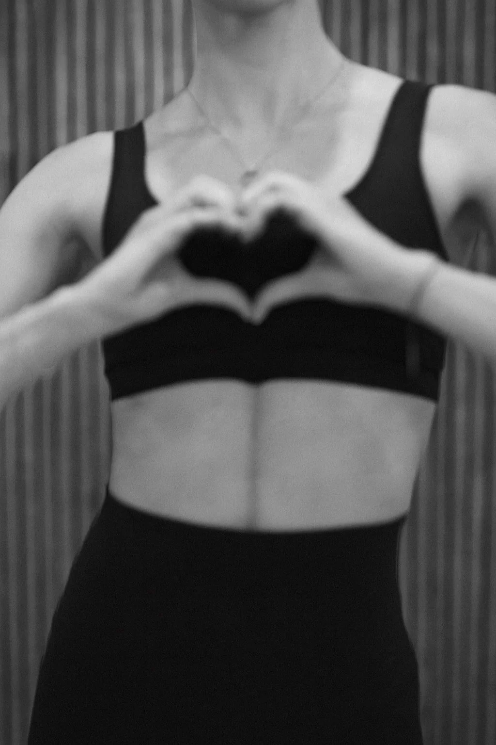 A woman in a sports bra making a heart shape with her hands.