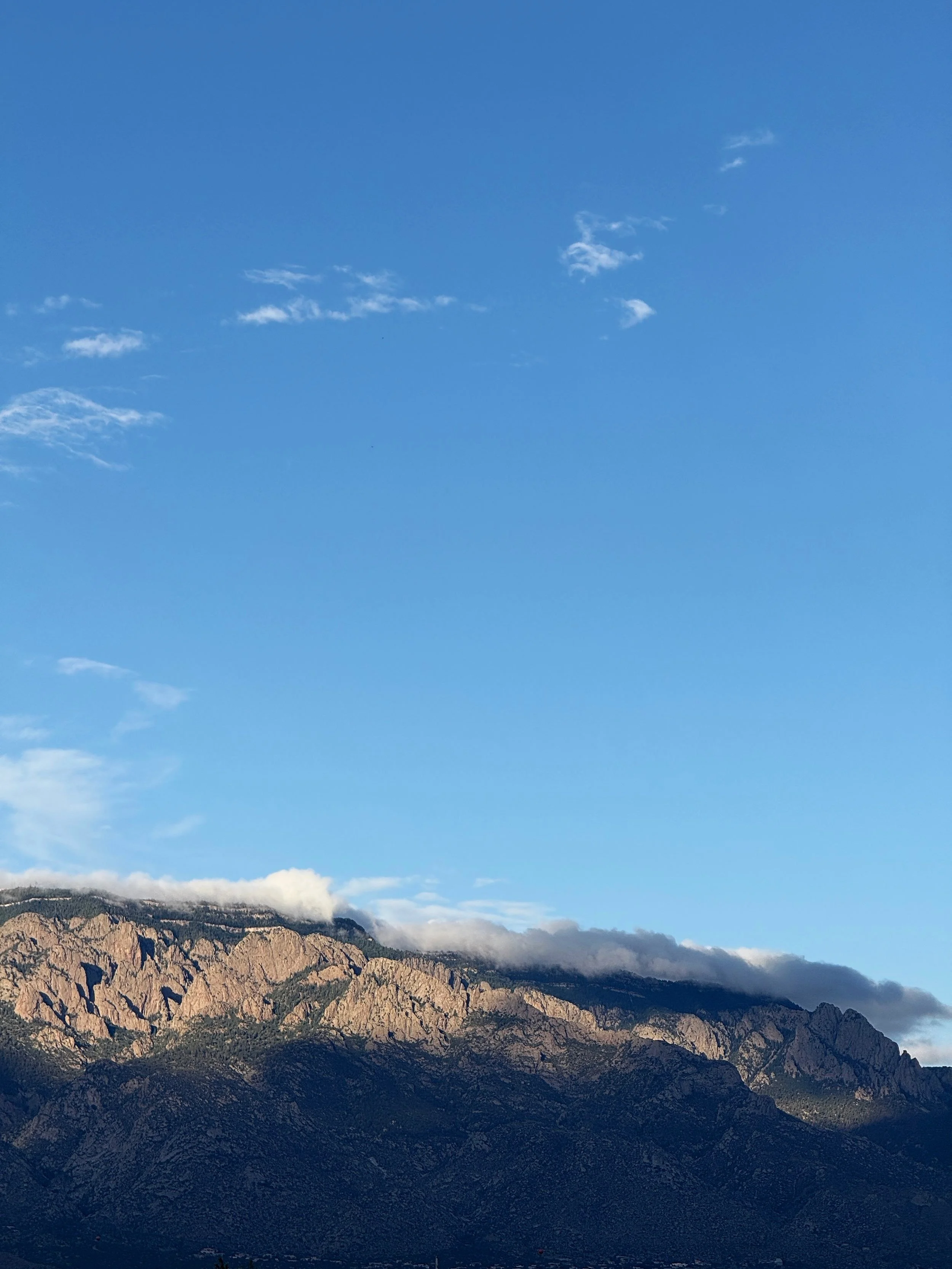 Mountain range with rocky peaks and a partly cloudy blue sky.
