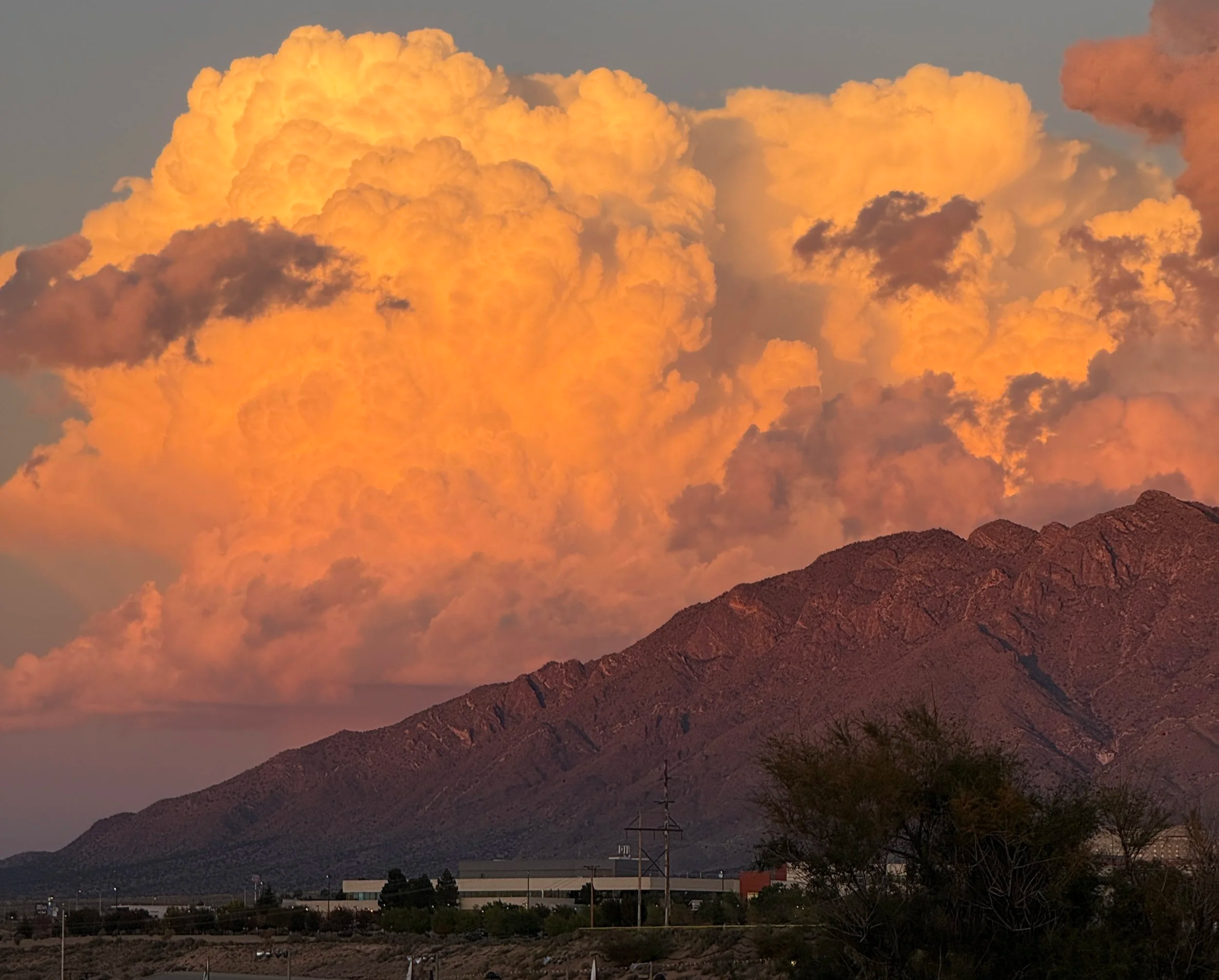 A mountain range with a large, vibrant orange and yellow cloud formation in the sky during sunset.