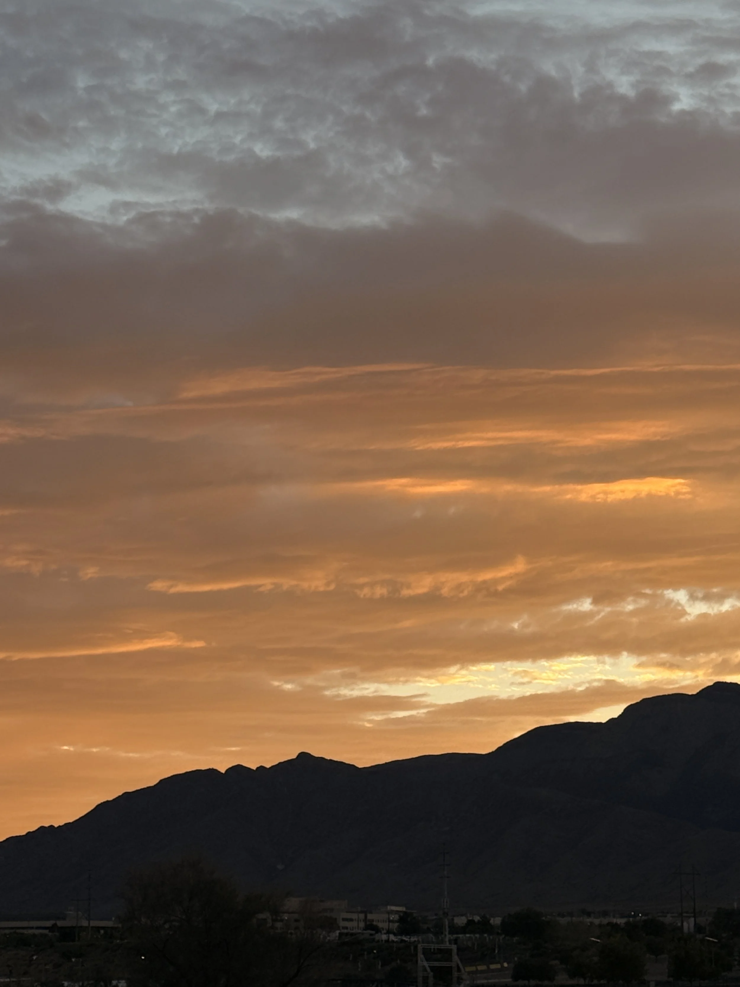 Sunset over mountains with orange and gray clouds in the sky.
