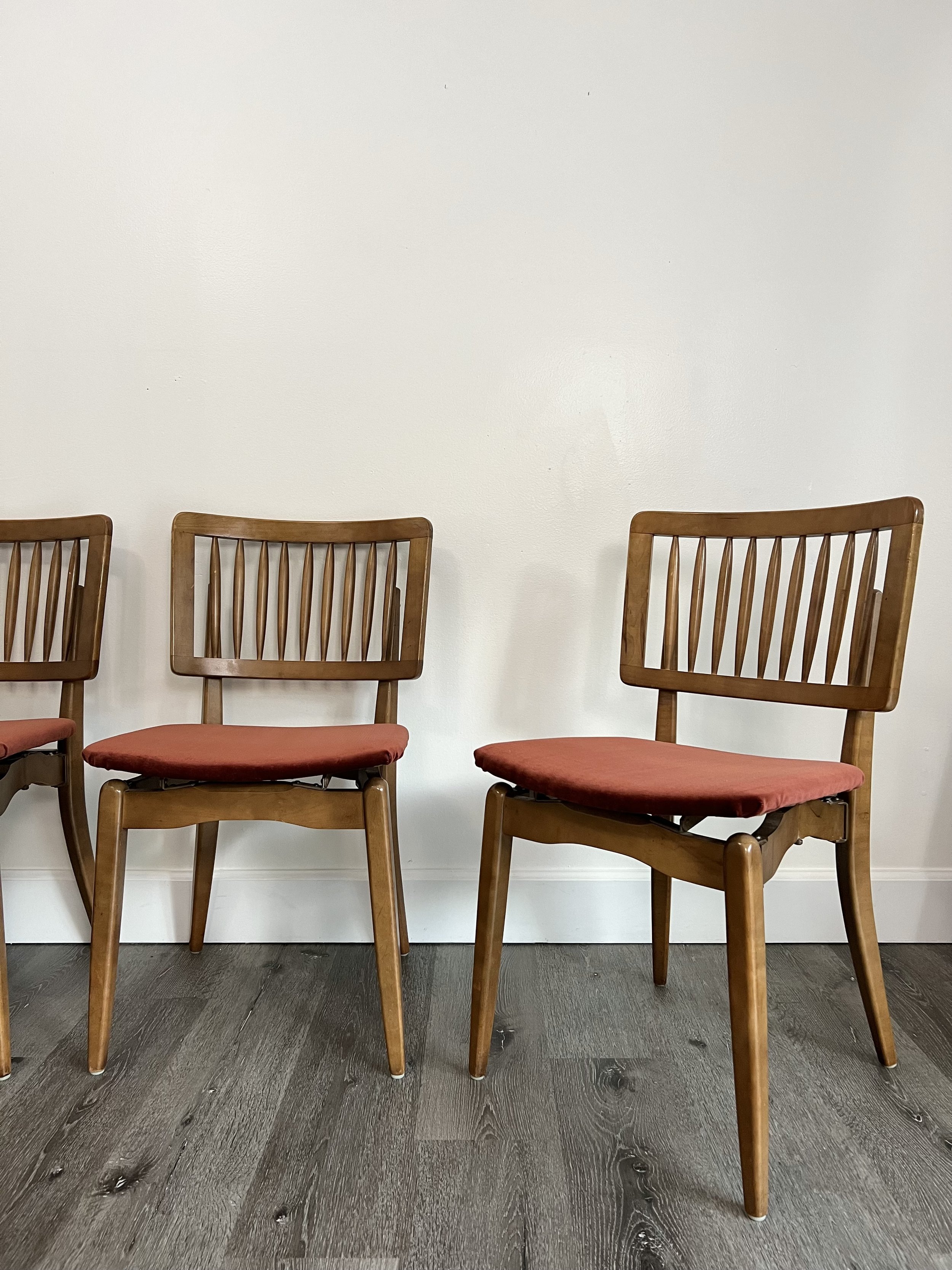 Pair of wooden chairs with slatted backs and red upholstered seats, placed against a plain white wall on dark wood flooring.