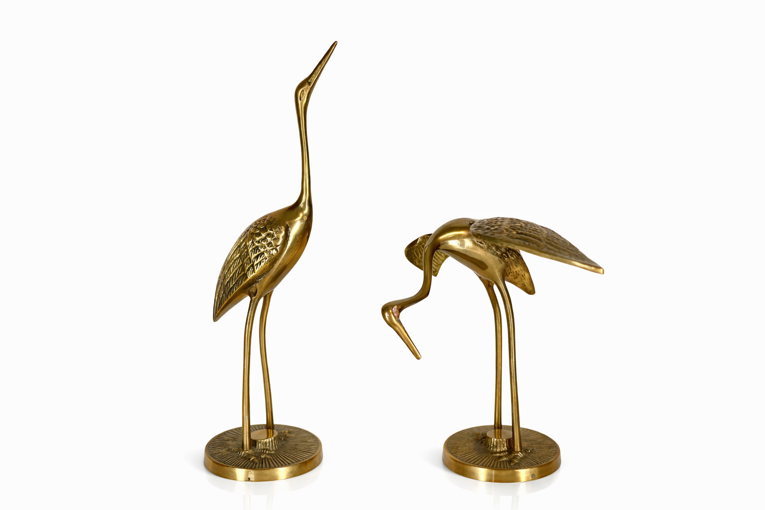 Decorative gold-colored sculptures of two herons, one standing and one bending down, on circular bases.